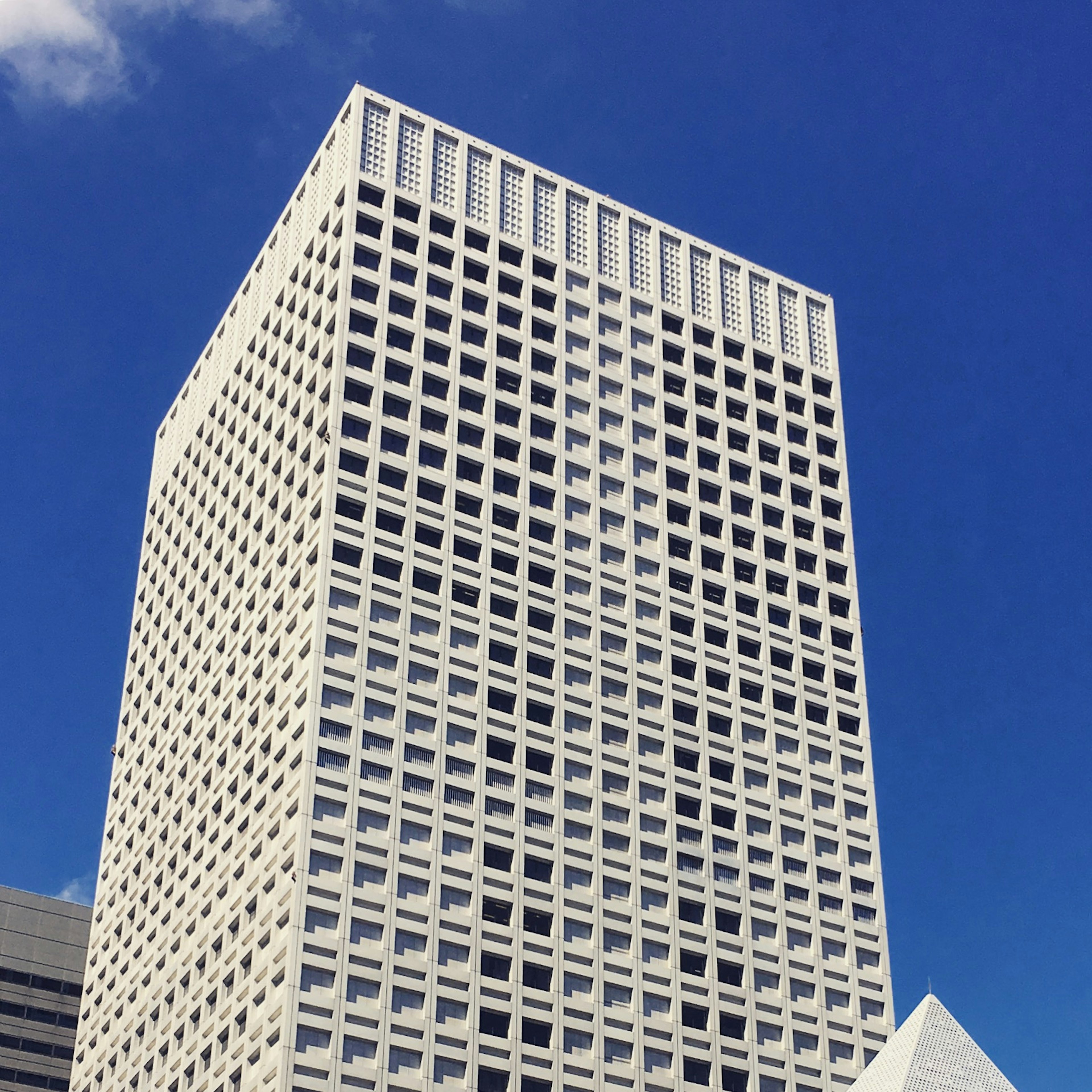 Tall white skyscraper with grid facade against blue sky