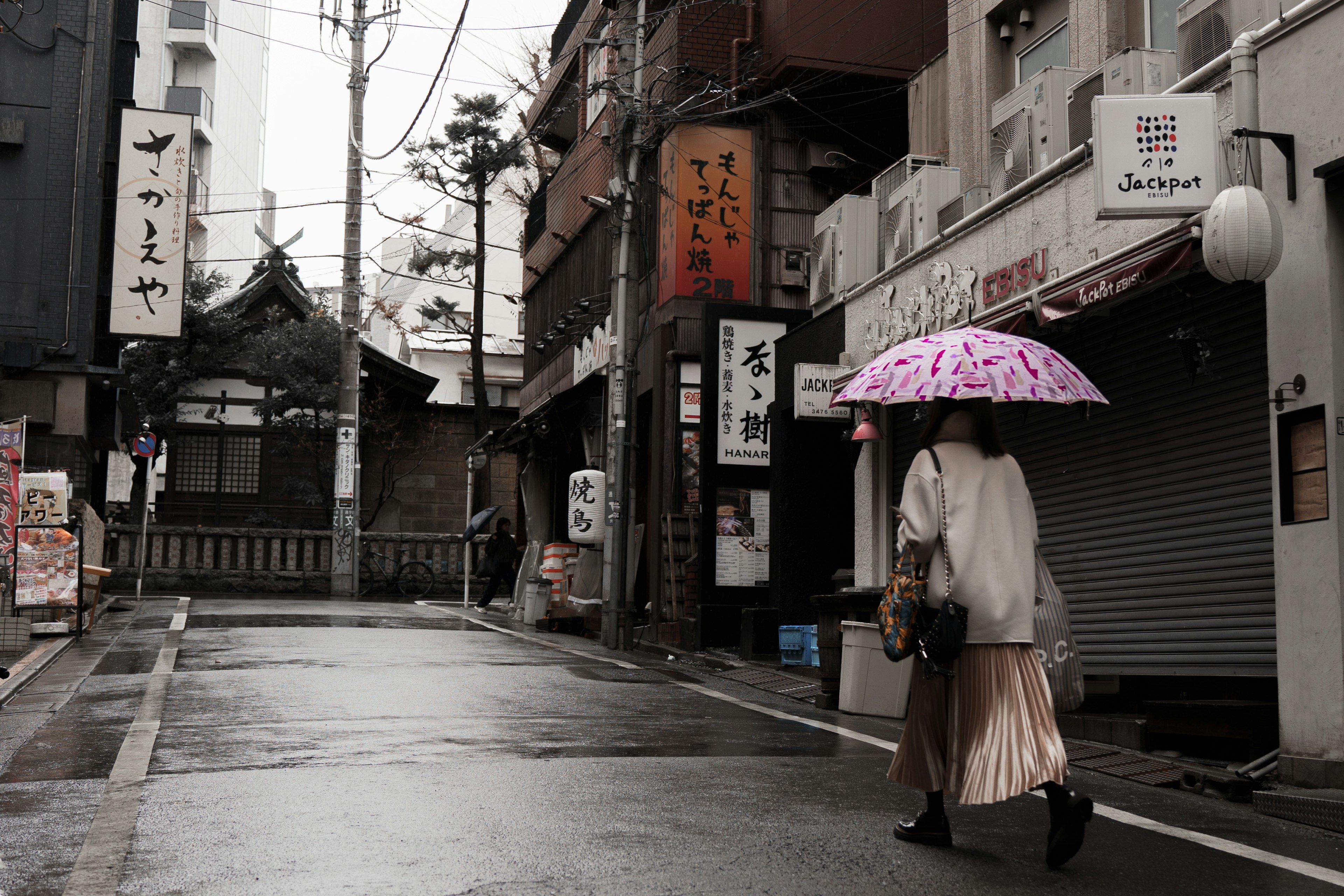 一位女性在雨中手持粉紅色雨傘走在安靜的街道上