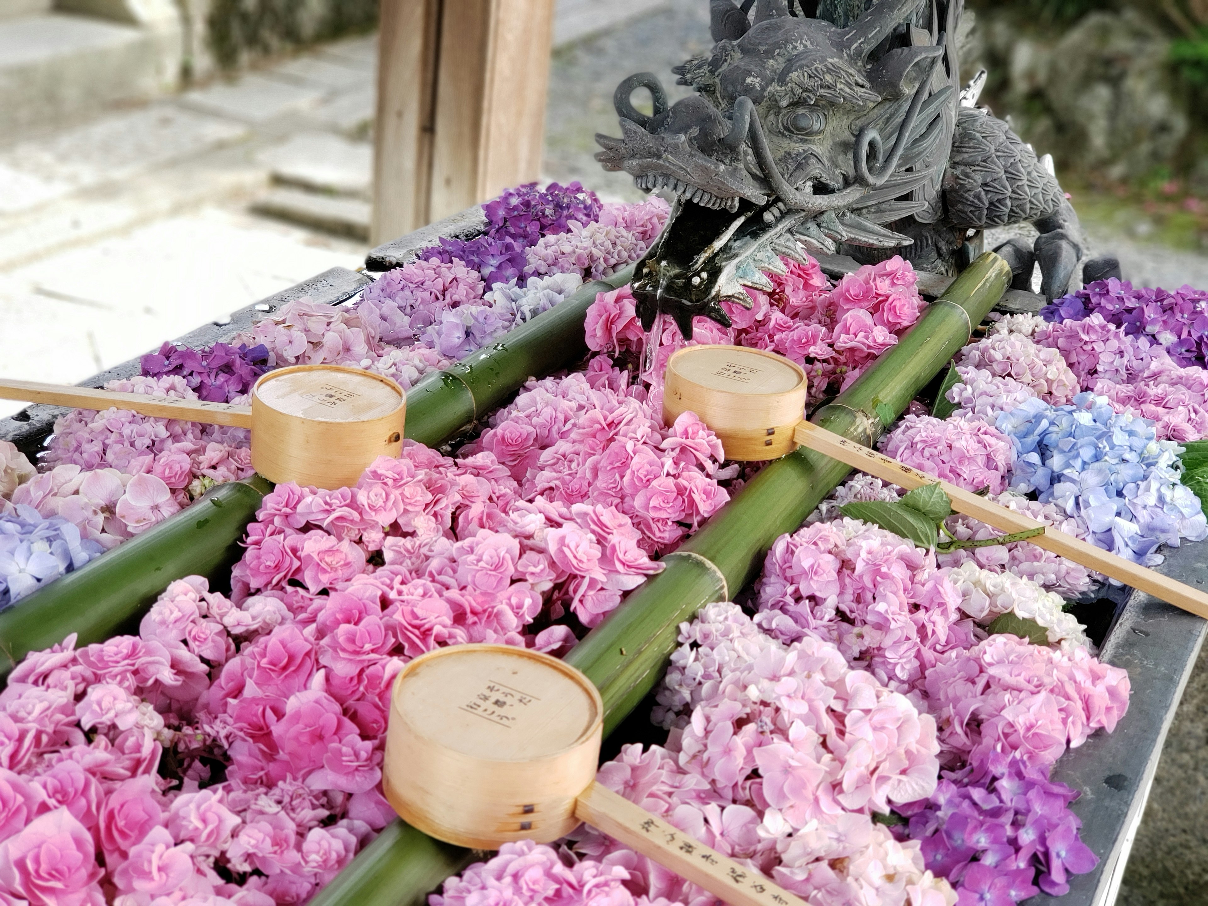 Sebuah patung naga di atas bak air yang didekorasi dengan bunga pink dan bambu