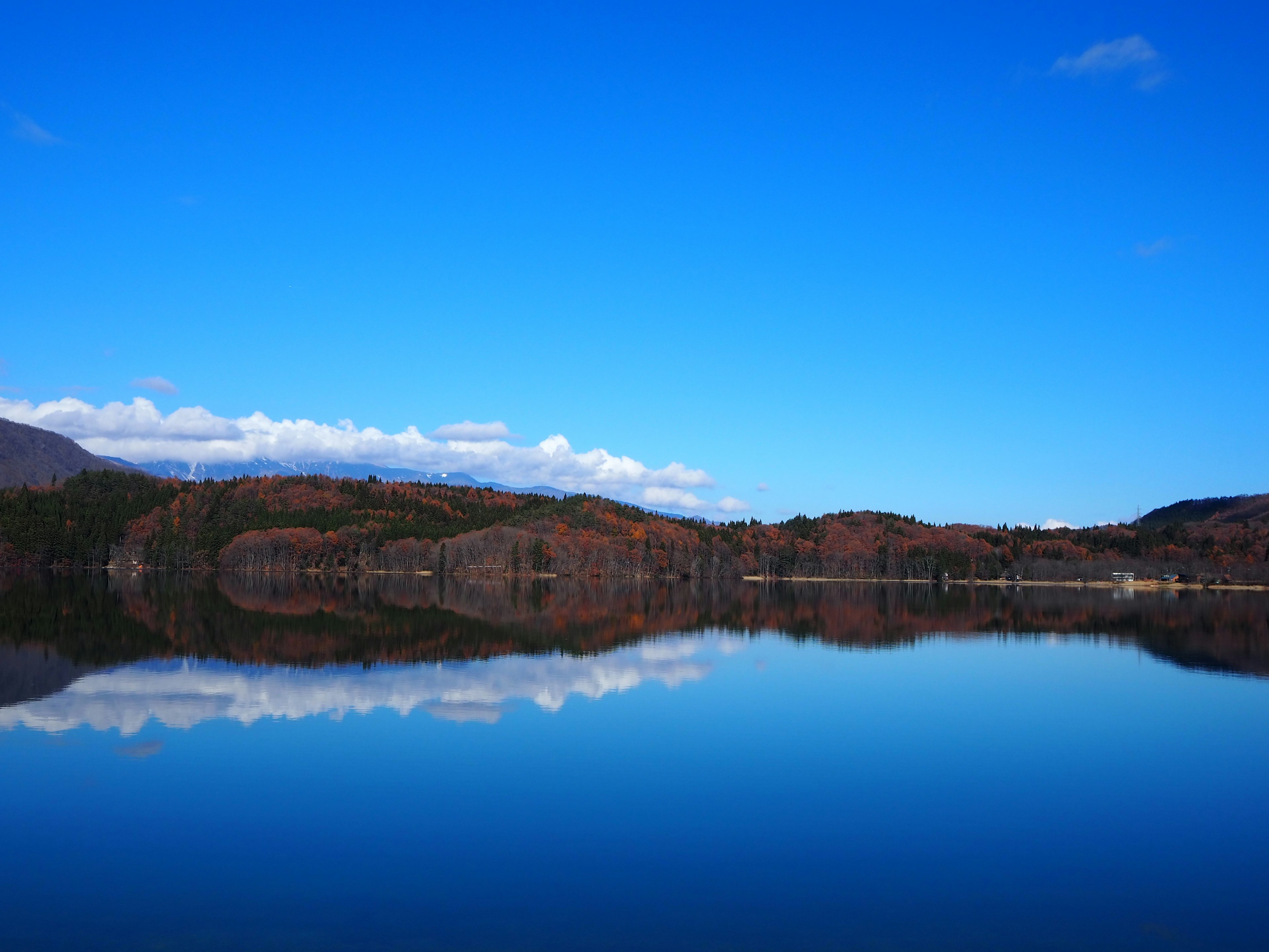 Danau tenang yang memantulkan langit biru dan pegunungan jauh