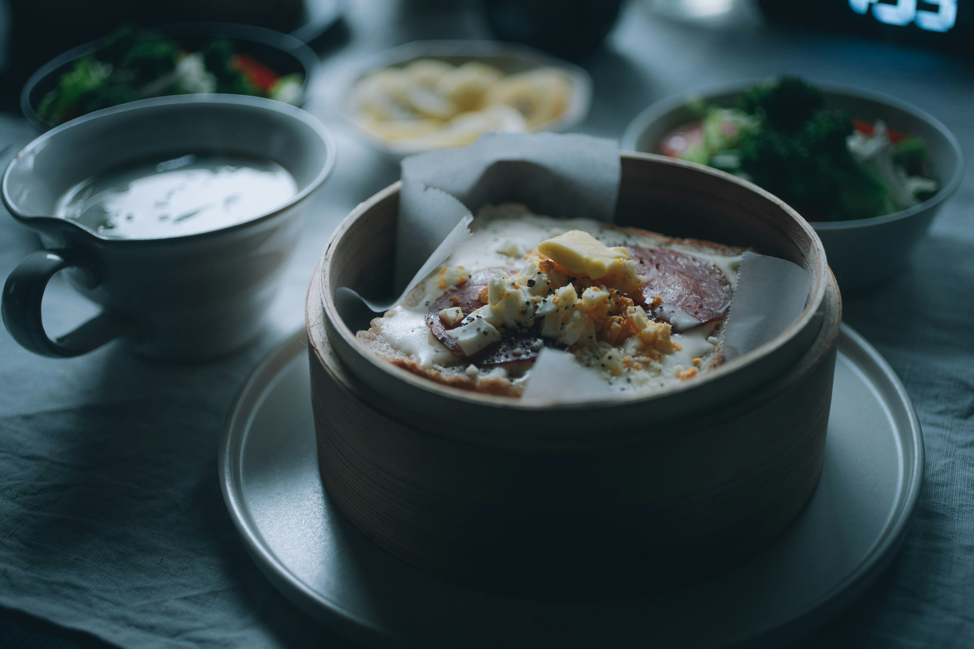 Un piatto al vapore in un cestello di bambù circondato da ciotole di zuppa e insalata