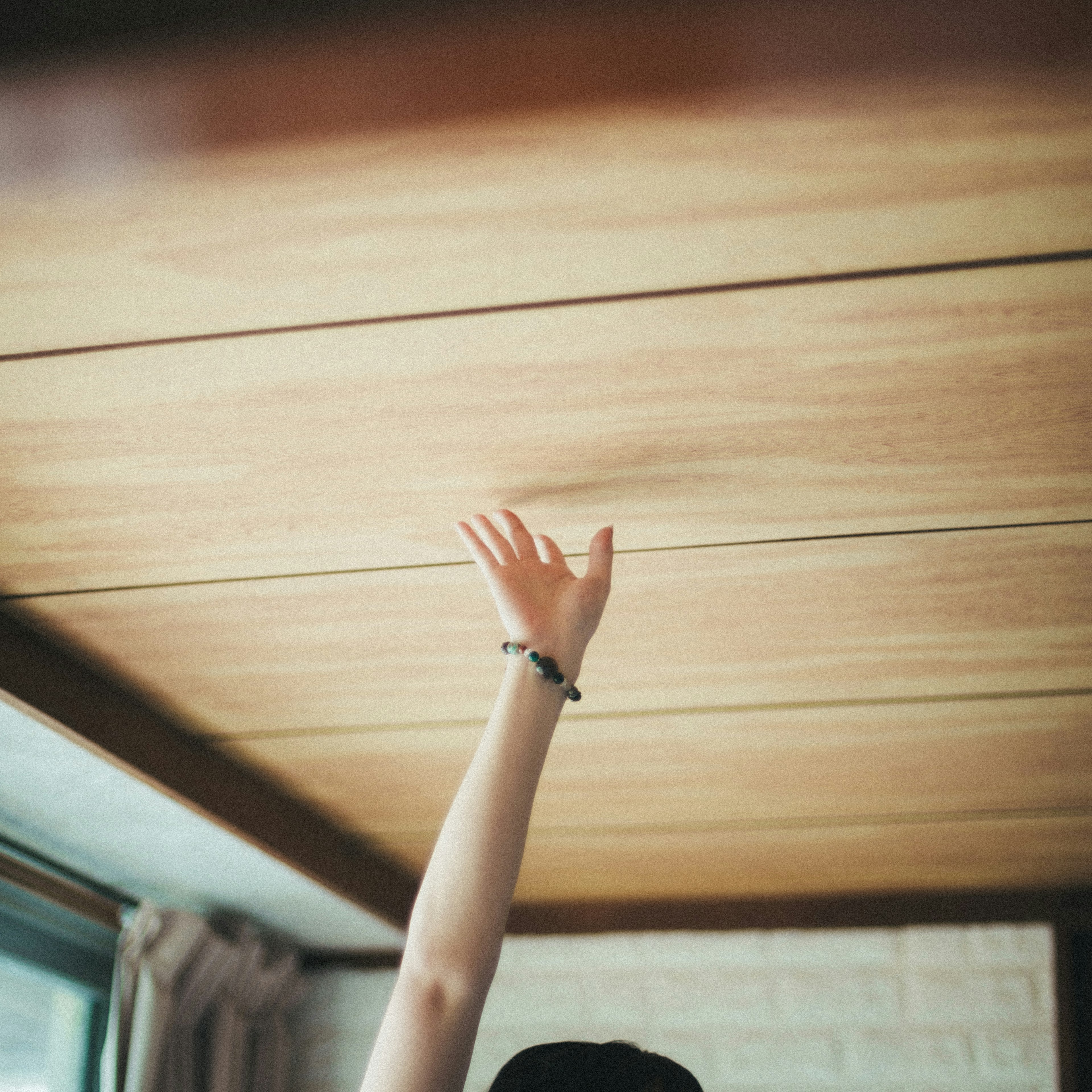 Le bras d'une personne levé sous un plafond en bois