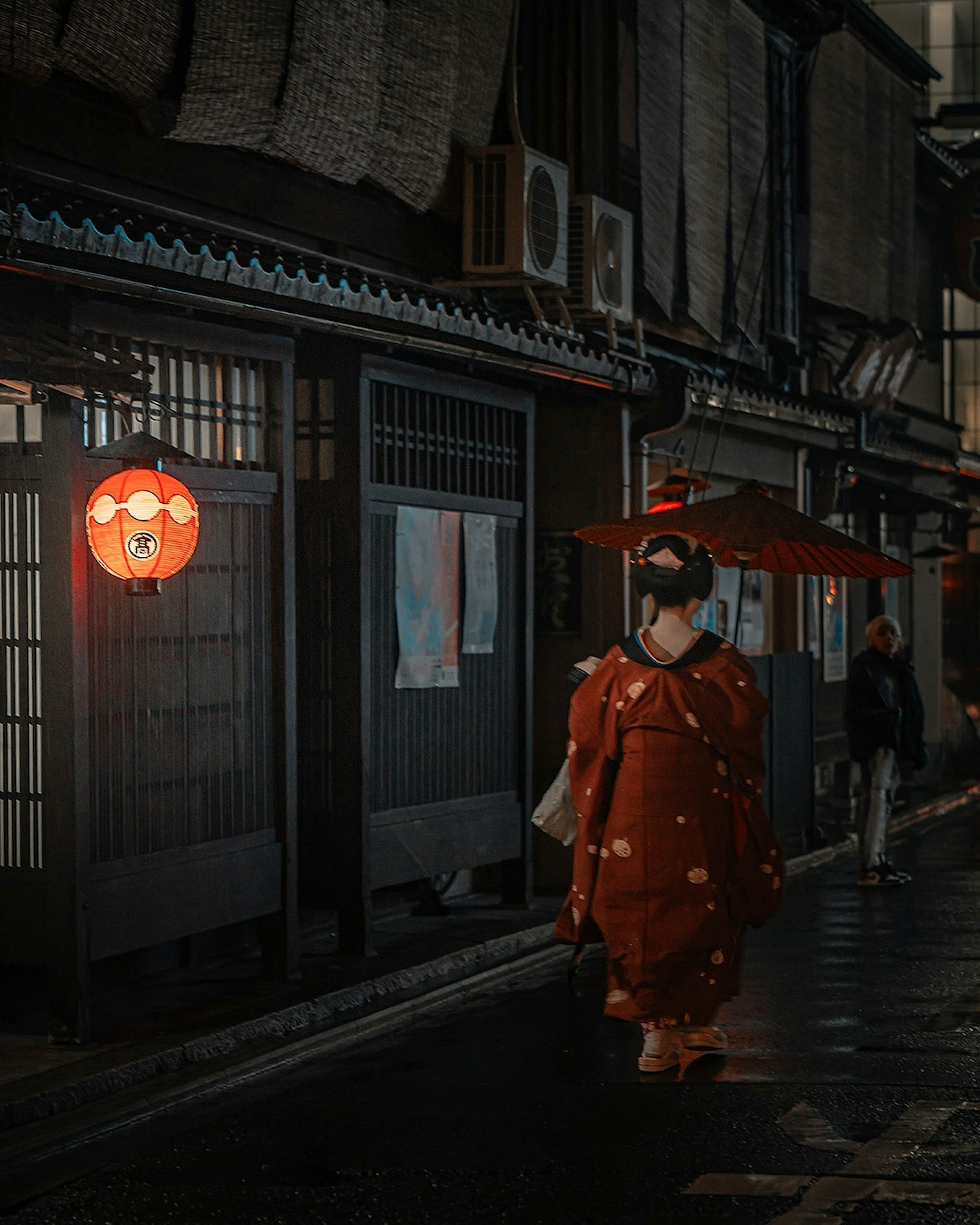 Una mujer en kimono caminando por una calle nocturna con una linterna roja