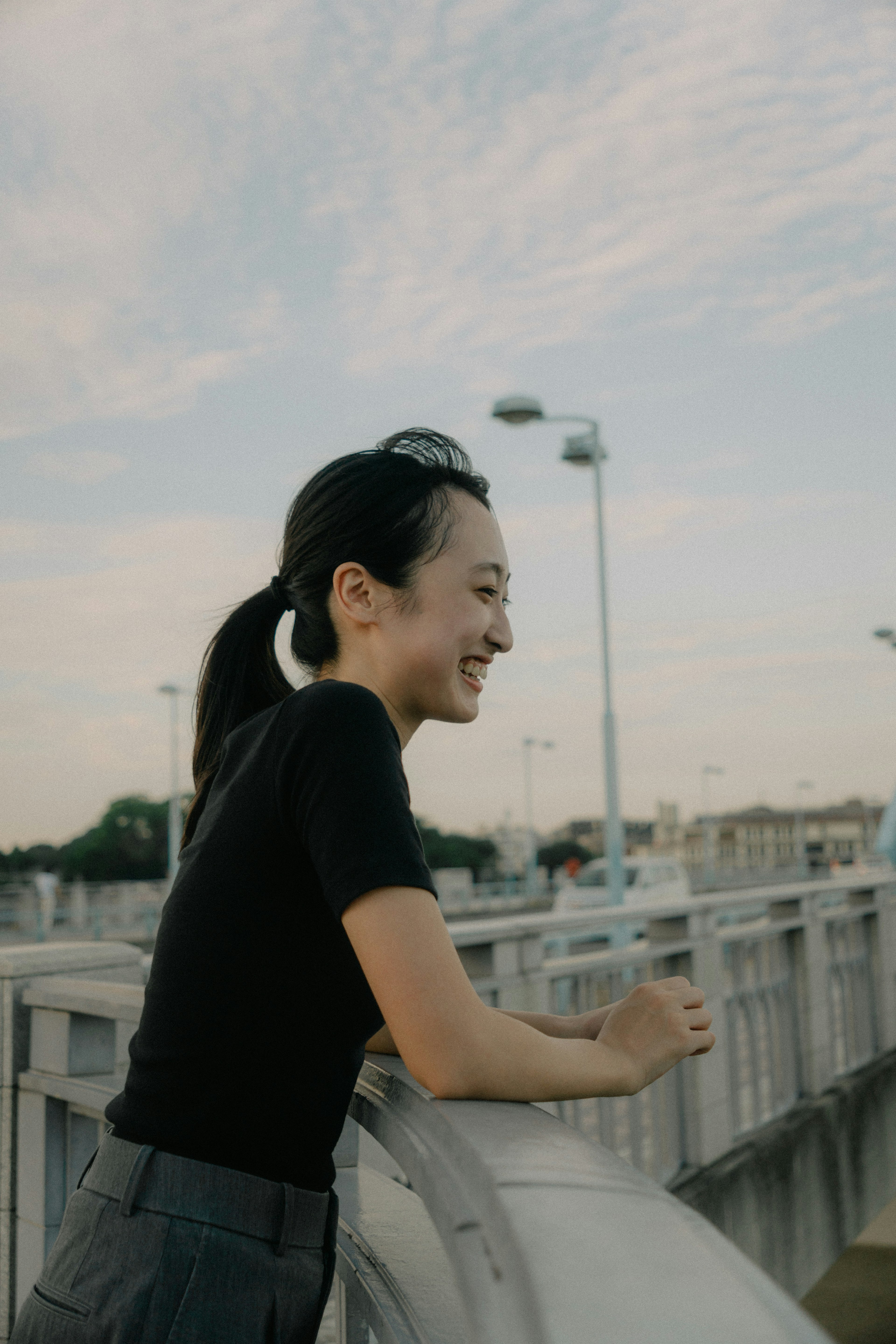 Profil latéral d'une femme souriante sur un pont avec ciel bleu