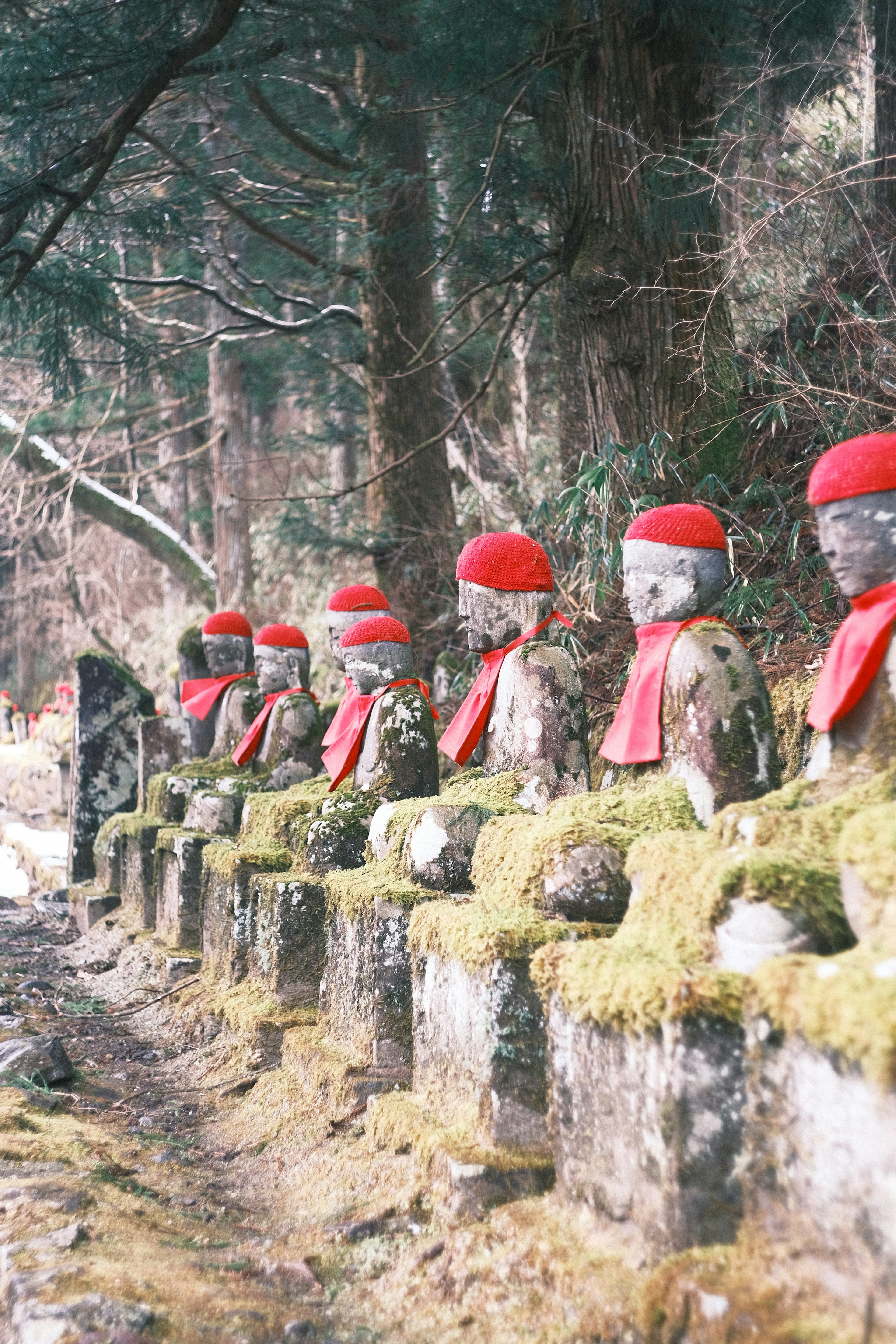 Fila de estatuas de piedra con sombreros y bufandas rojas rodeadas de vegetación