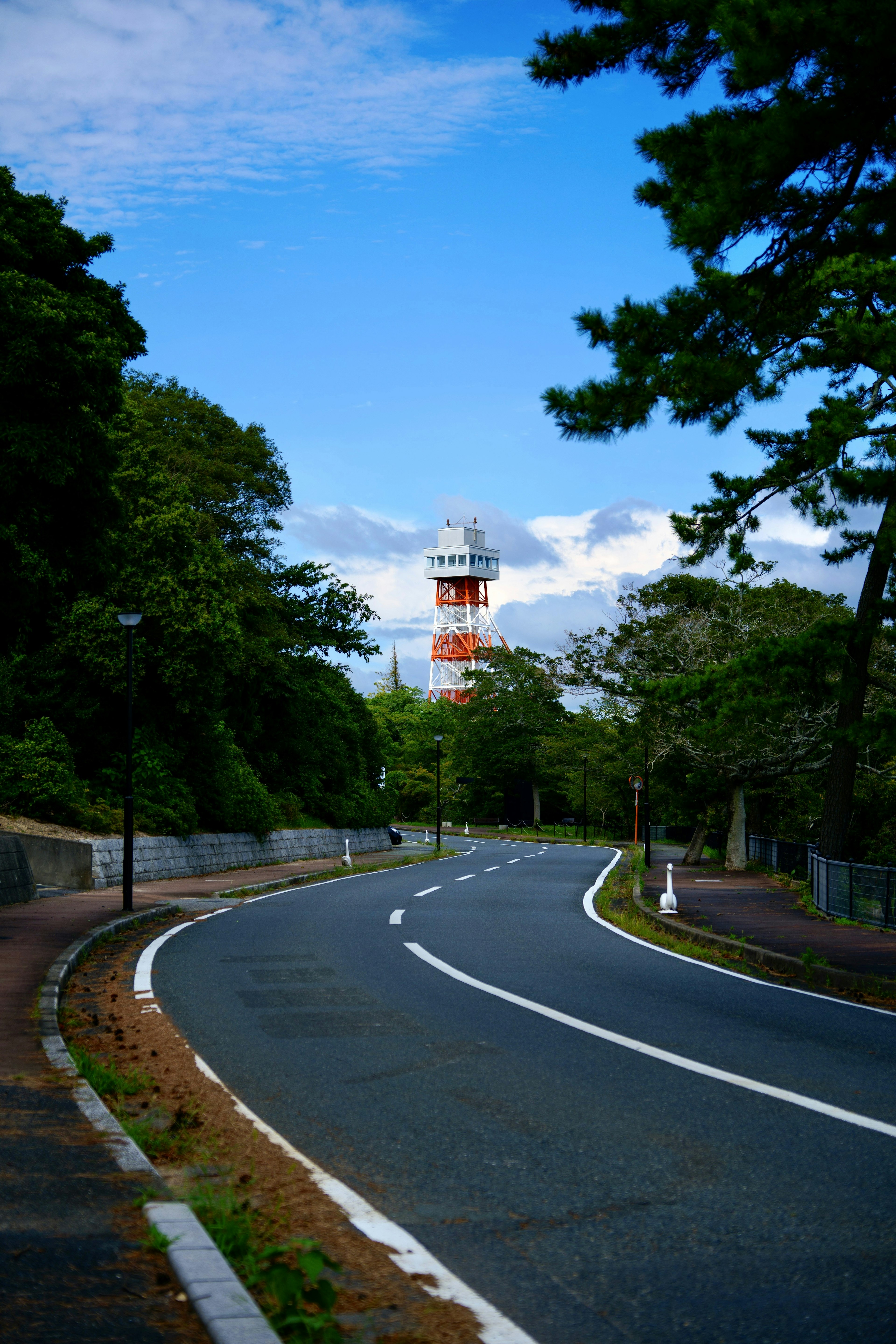 Scenic road winding through lush greenery with a lighthouse in the background