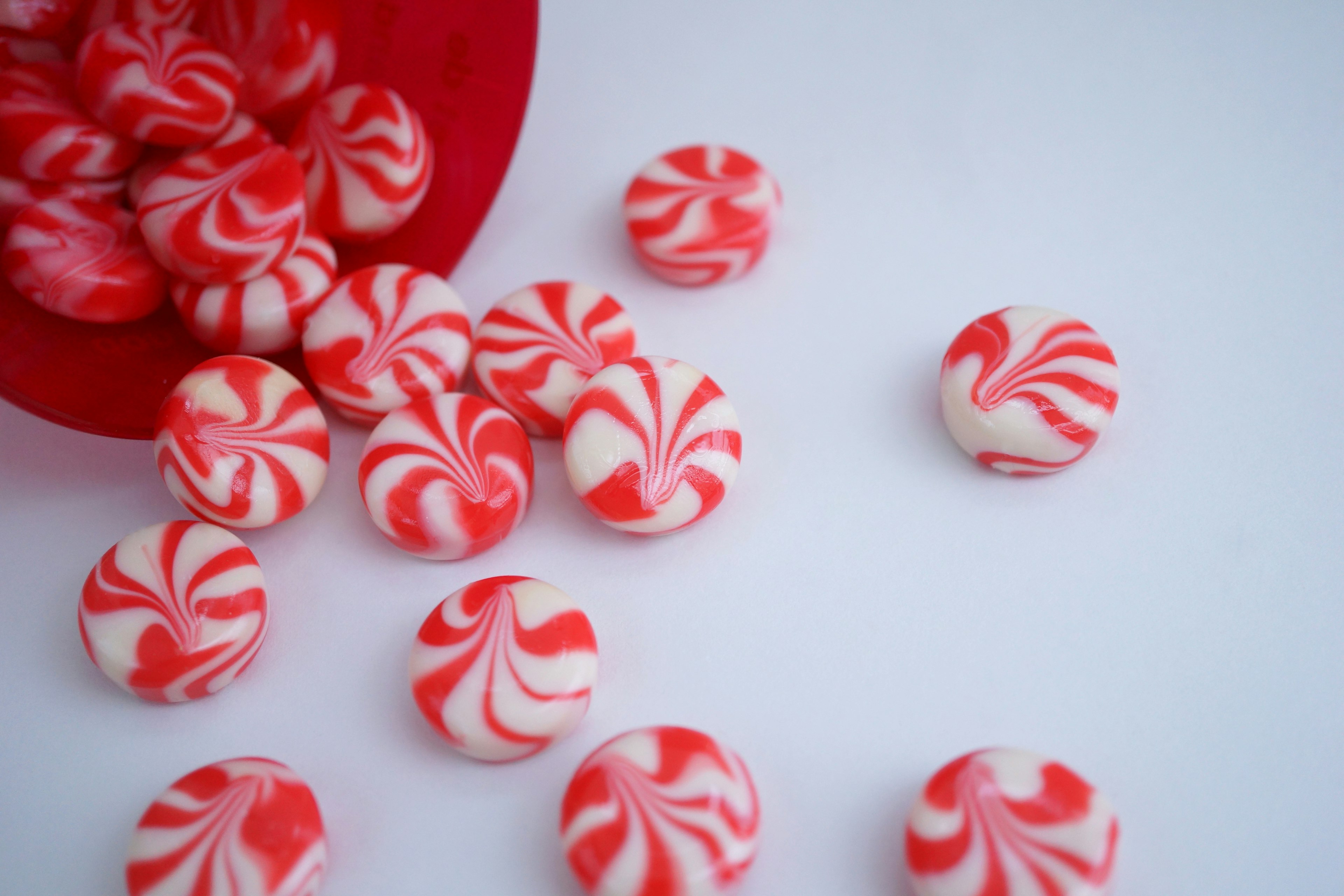 Caramelos de rayas rojas y blancas esparcidos sobre una superficie blanca