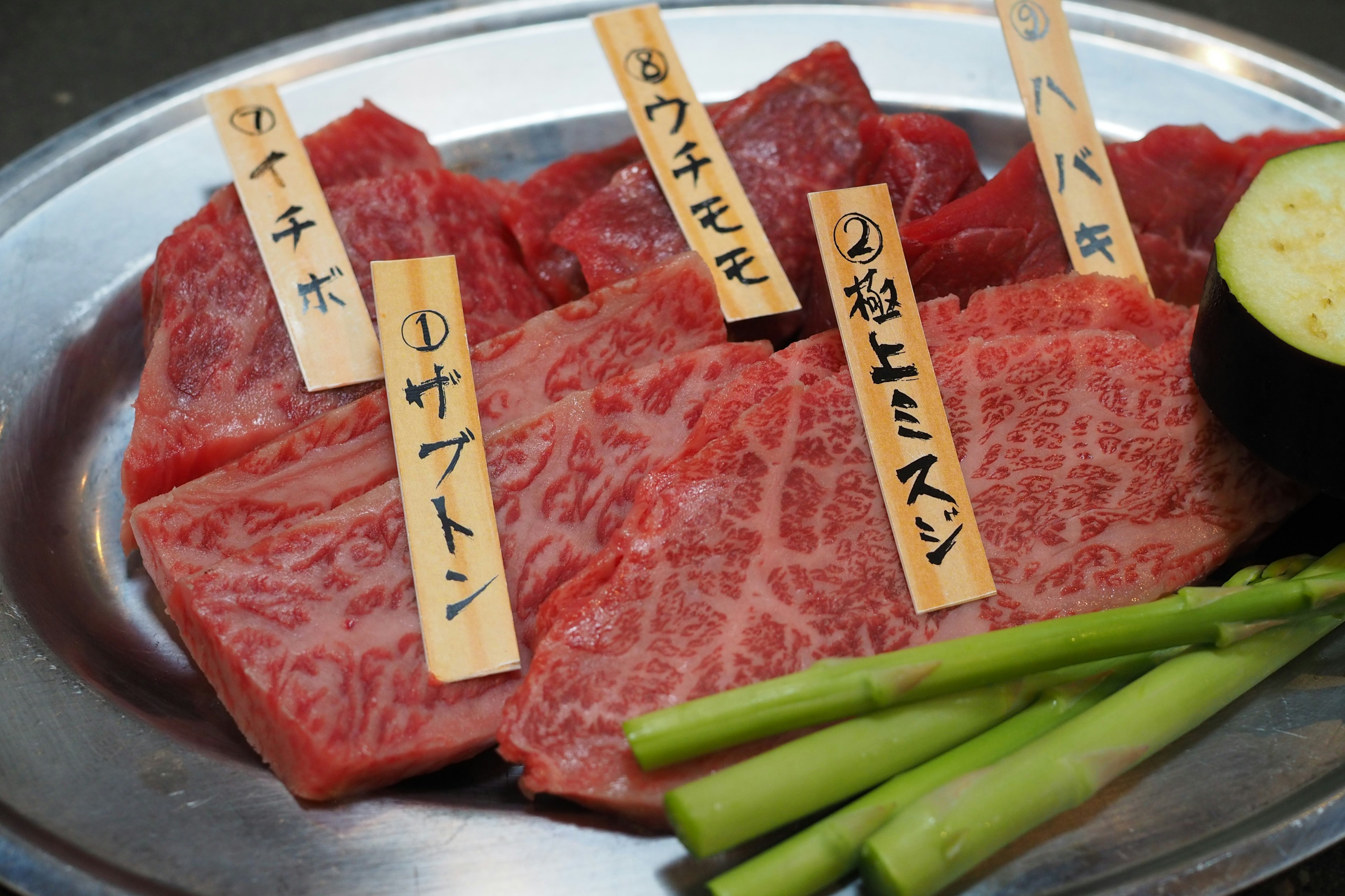 Tranches de bœuf Wagyu japonais de qualité disposées sur un plat en argent avec des étiquettes japonaises indiquant différentes coupes