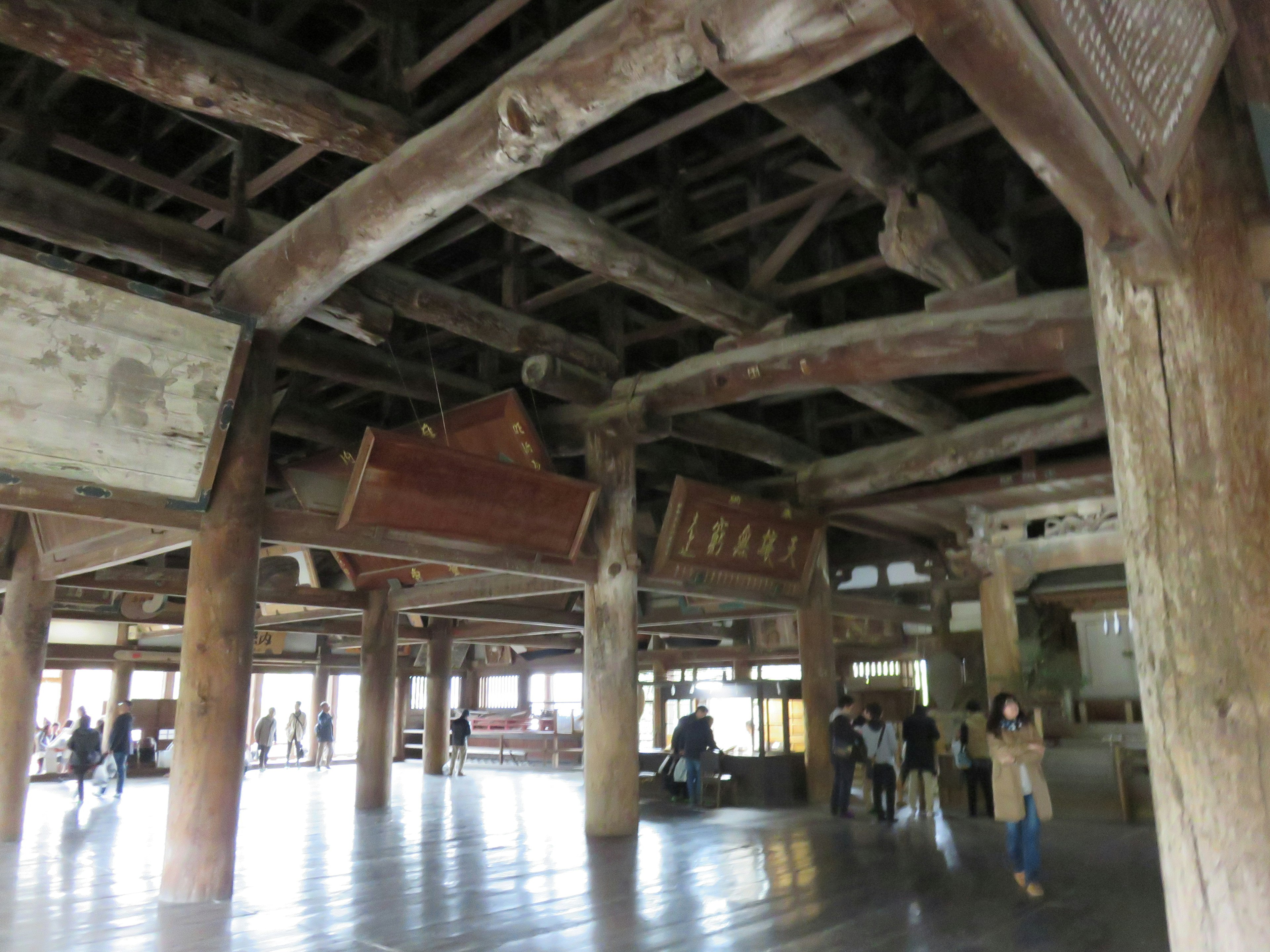 Interior de una antigua estructura de madera con vigas expuestas y letreros colgantes con visitantes