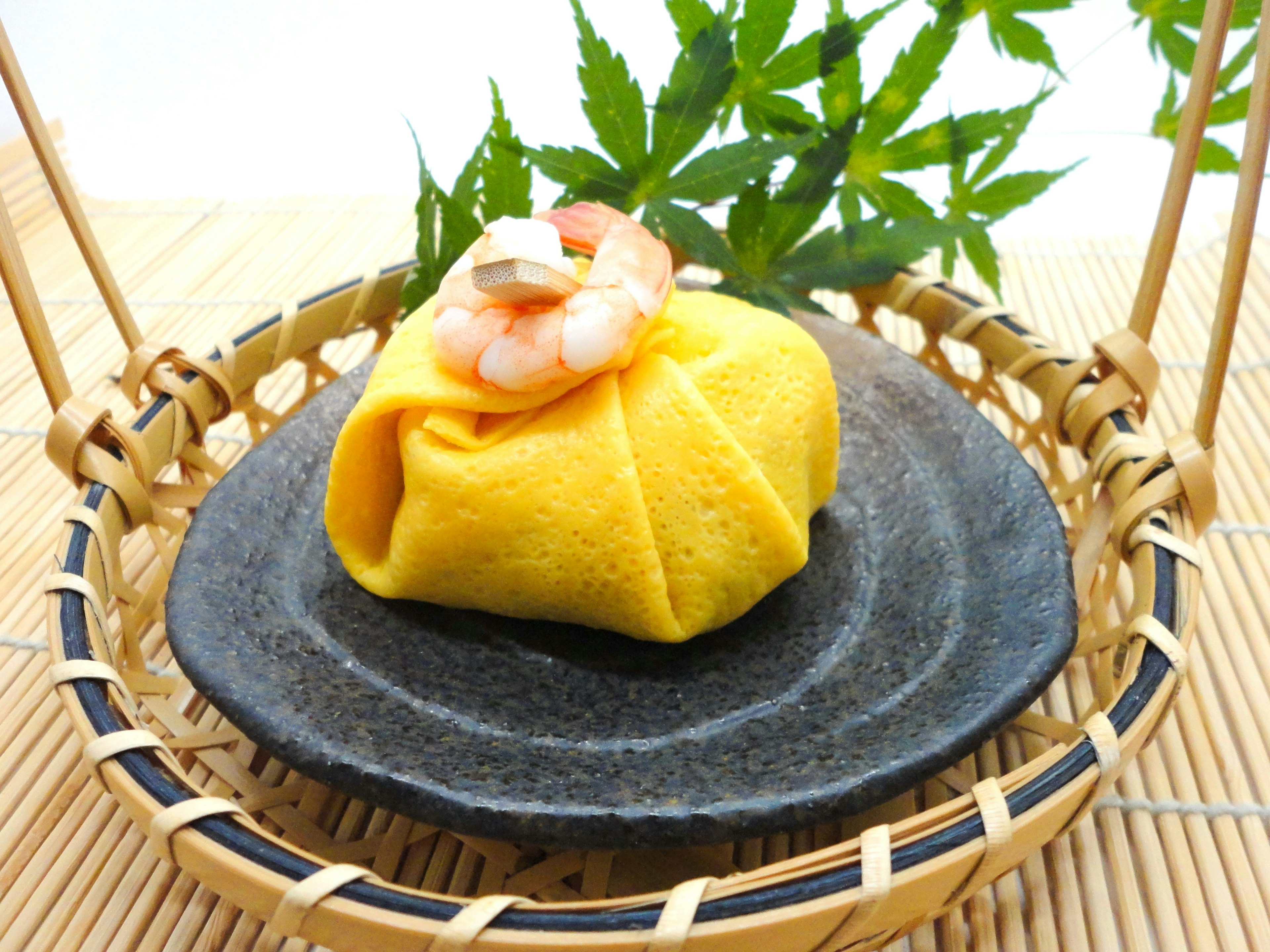 Hermosa presentación de la cocina japonesa con un envoltorio amarillo cubierto de camarones y una hoja