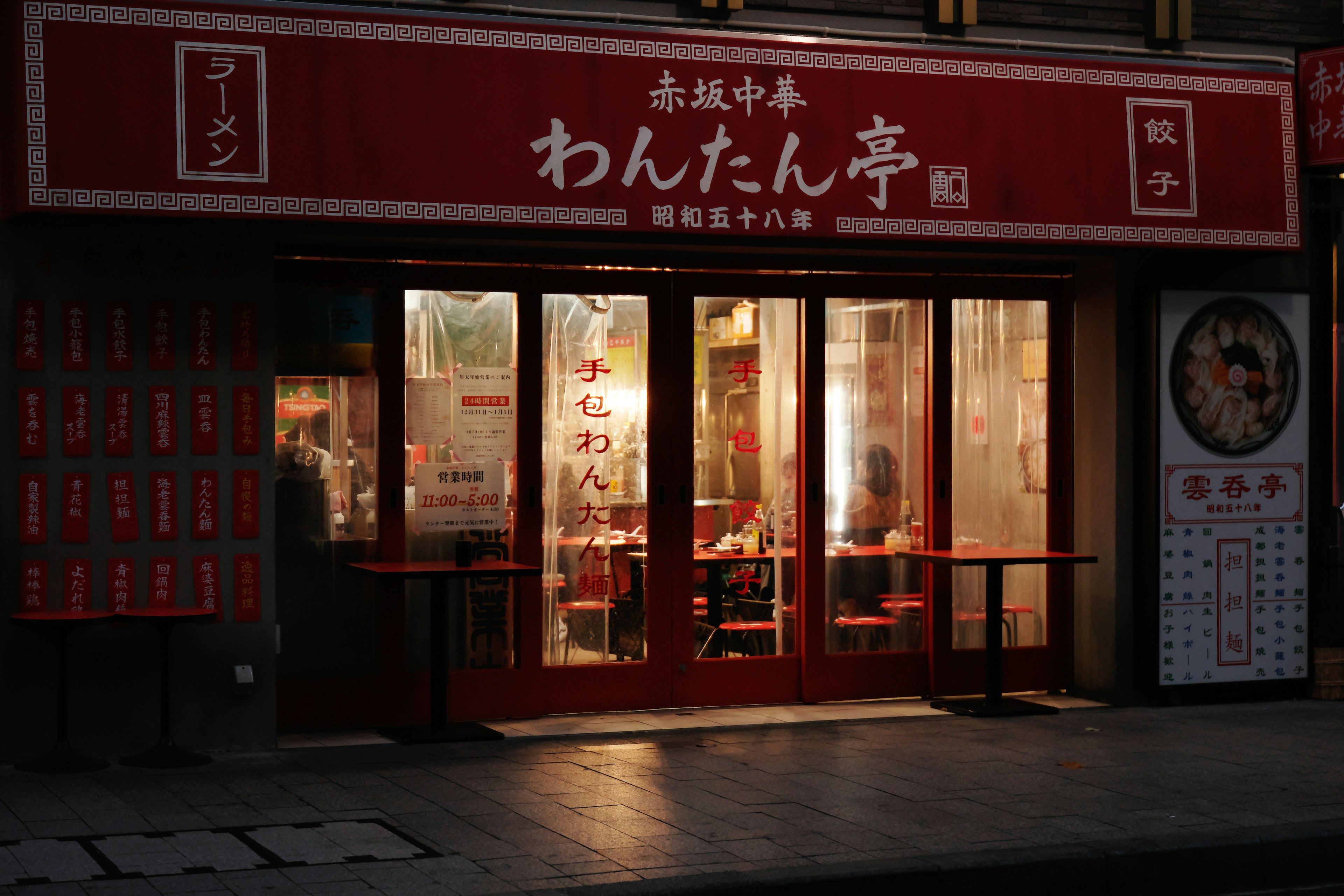 Außenansicht eines chinesischen Restaurants mit rotem Schild beleuchtete Fenster zeigen Tische und Stühle