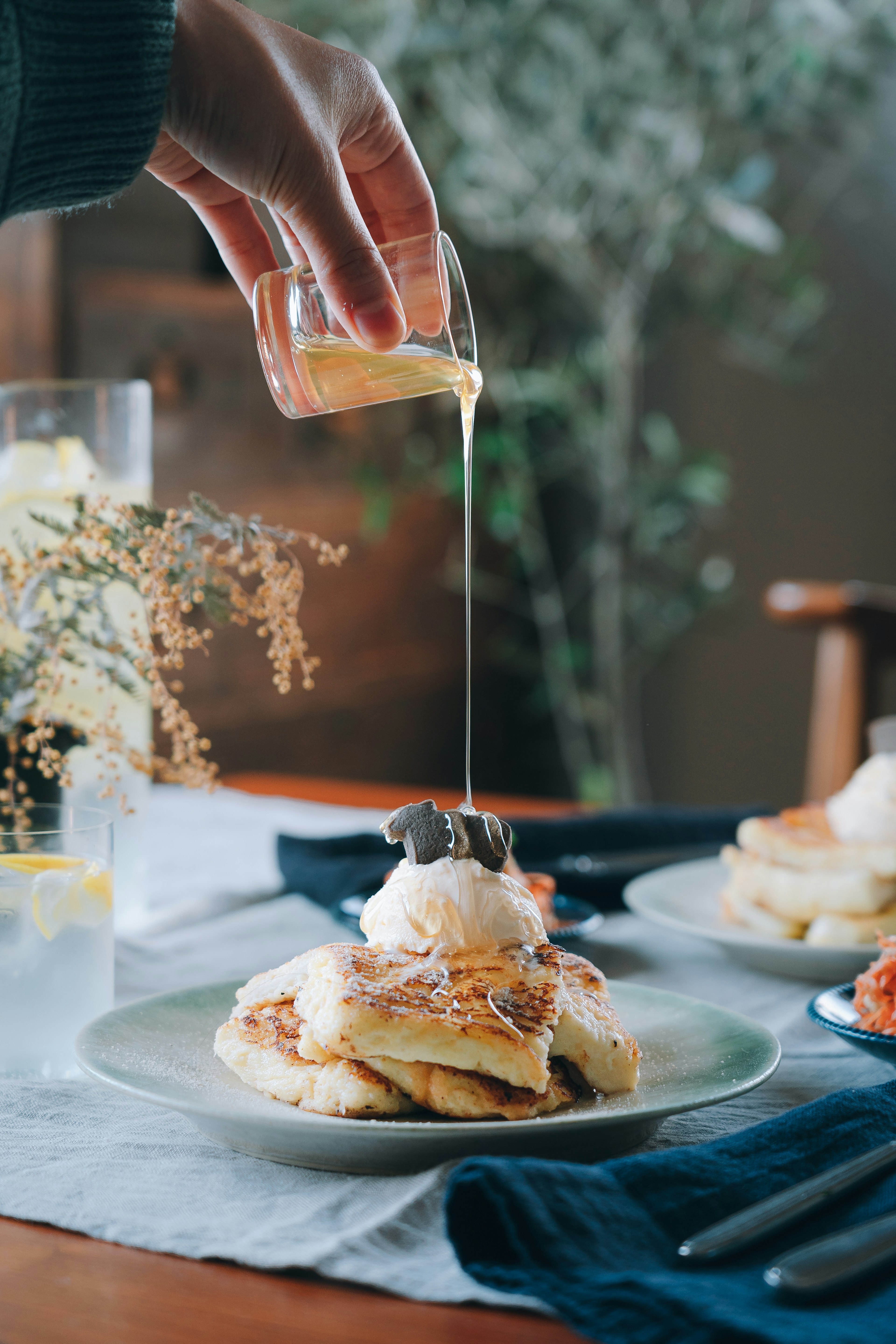 A hand pouring maple syrup over pancakes with ice cream