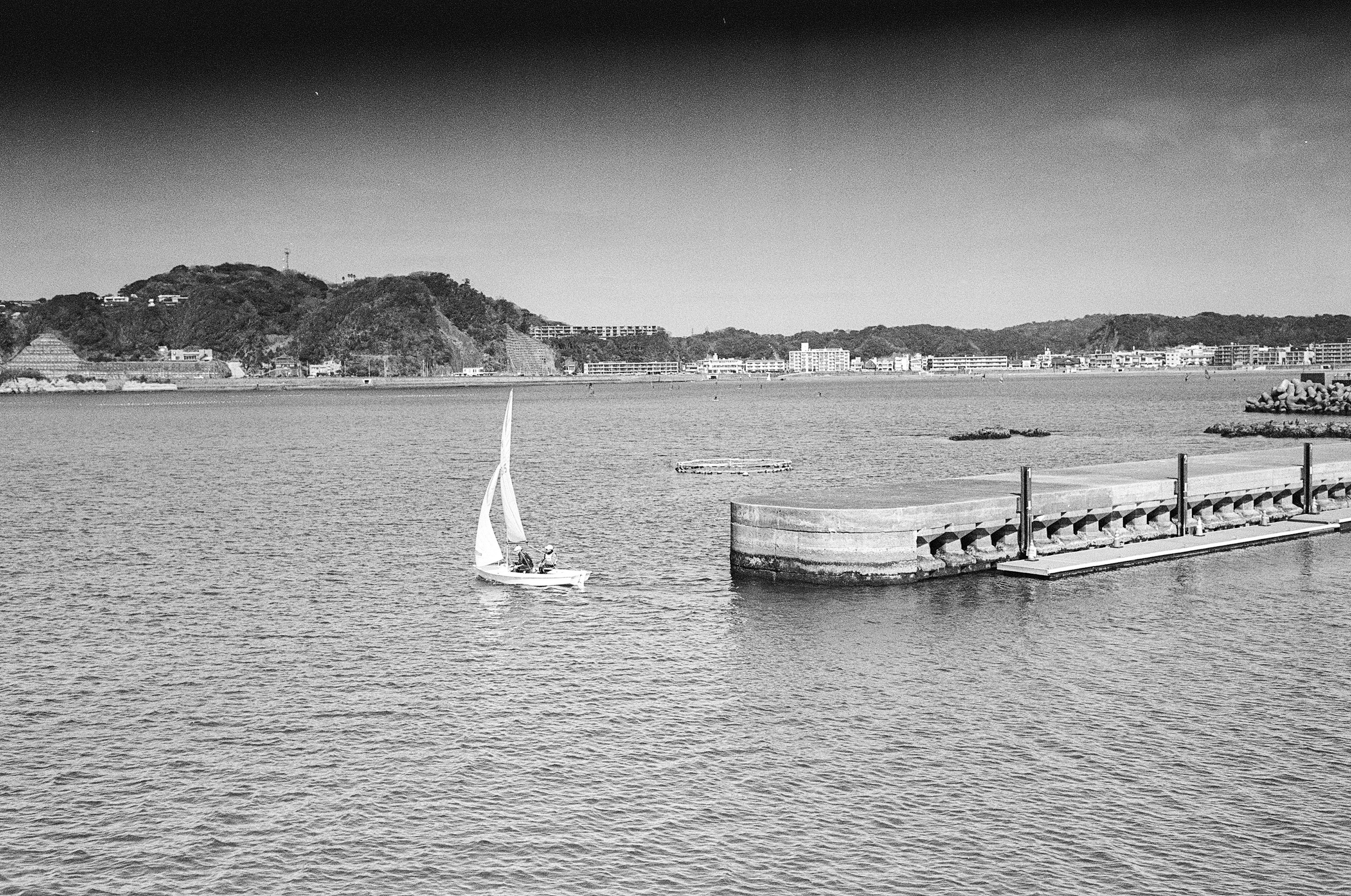 A small sailboat on the black and white sea with a dock