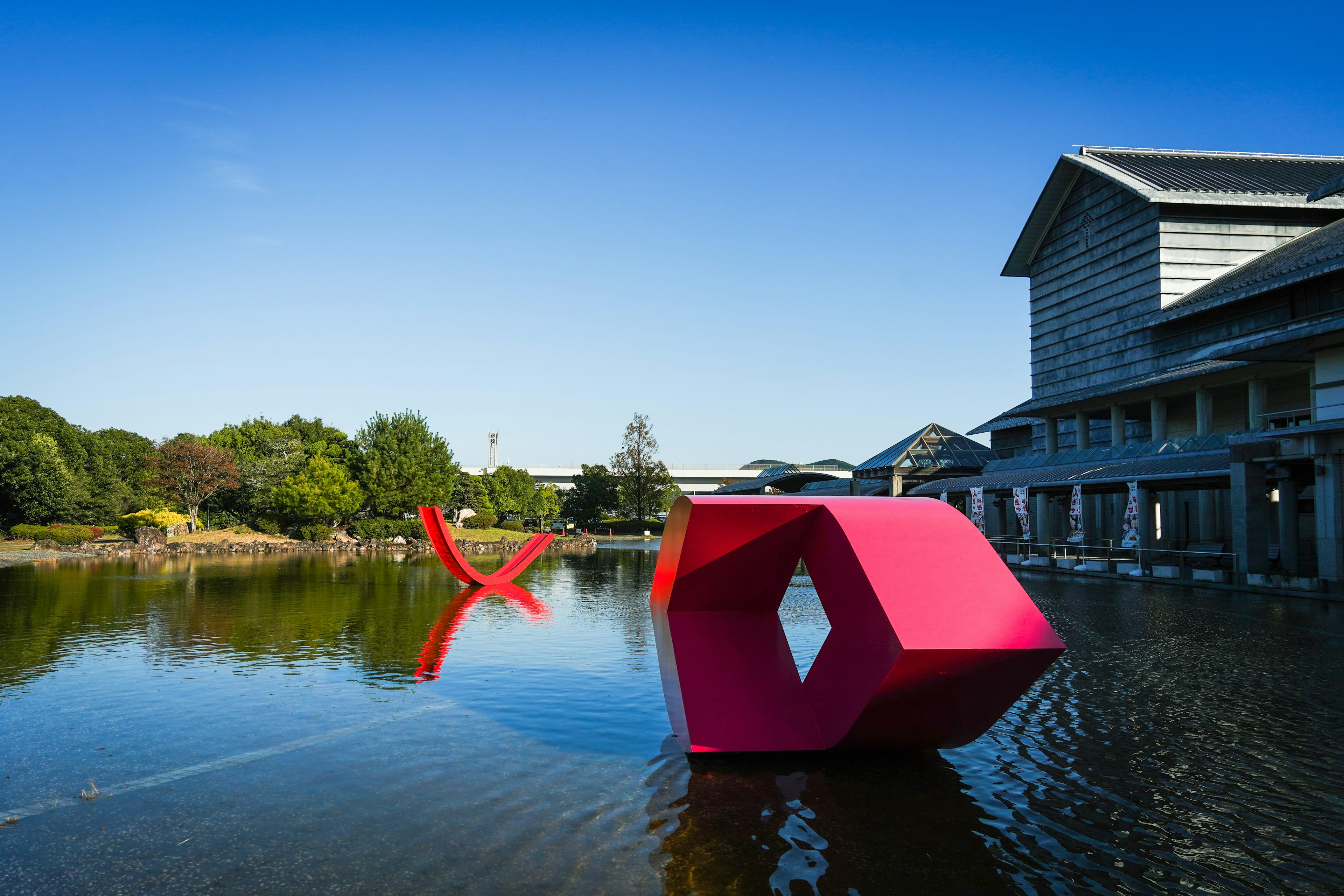 Sculptures rouges flottant sur l'eau avec un bâtiment moderne en arrière-plan