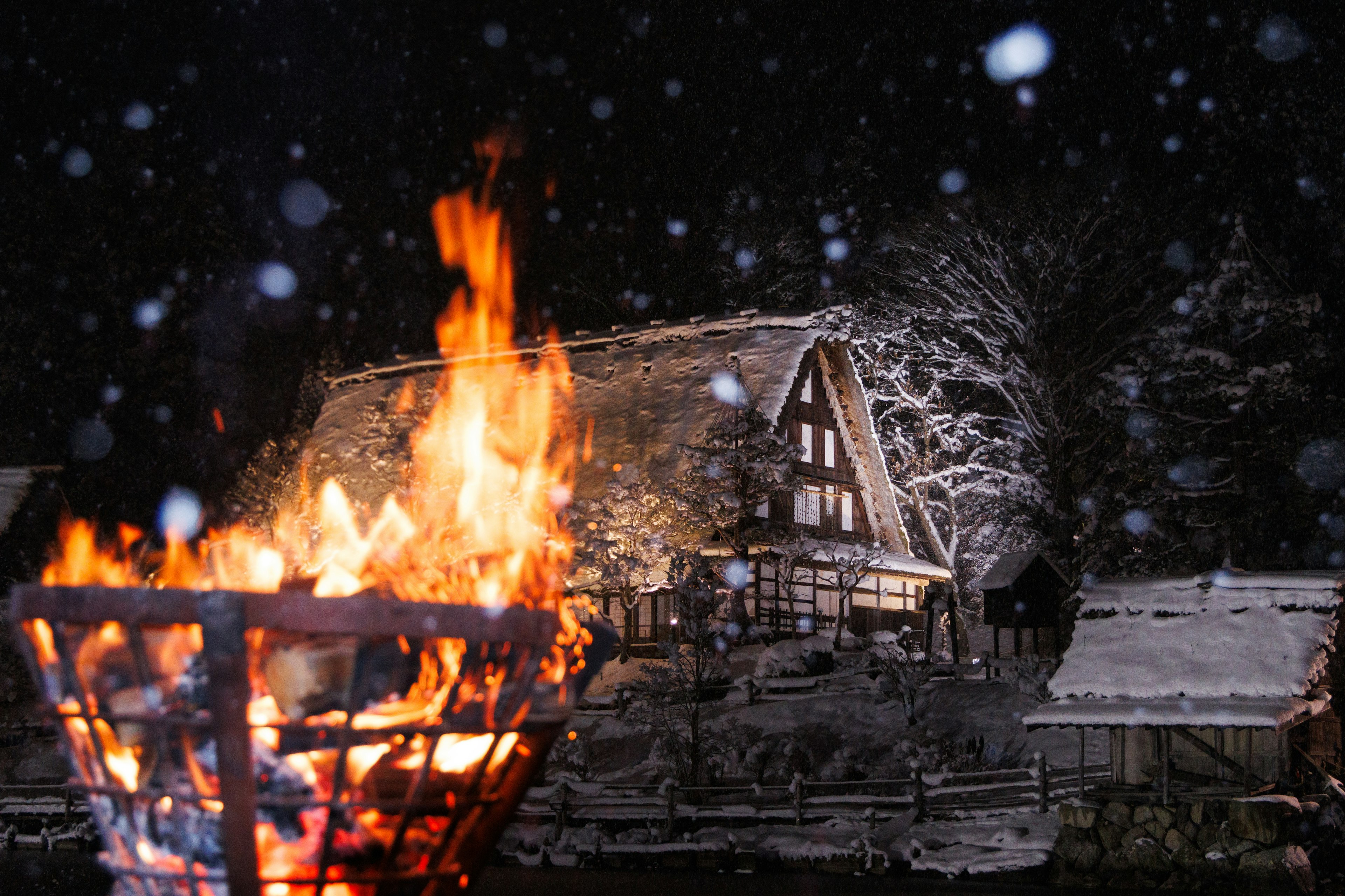 夜の雪の中で燃える焚き火と雪に覆われた家