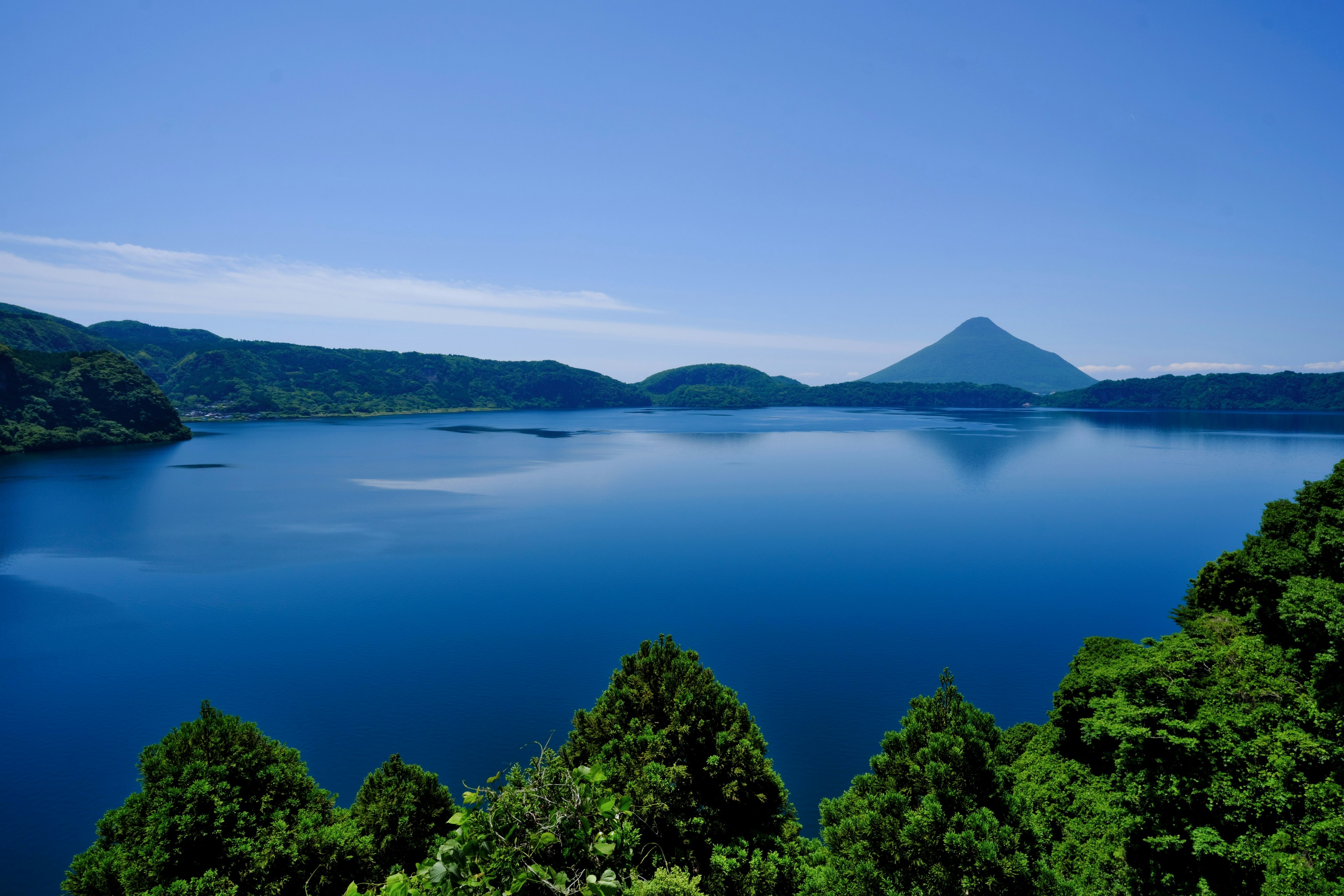 Pemandangan indah danau dikelilingi gunung dengan langit biru dan pepohonan hijau