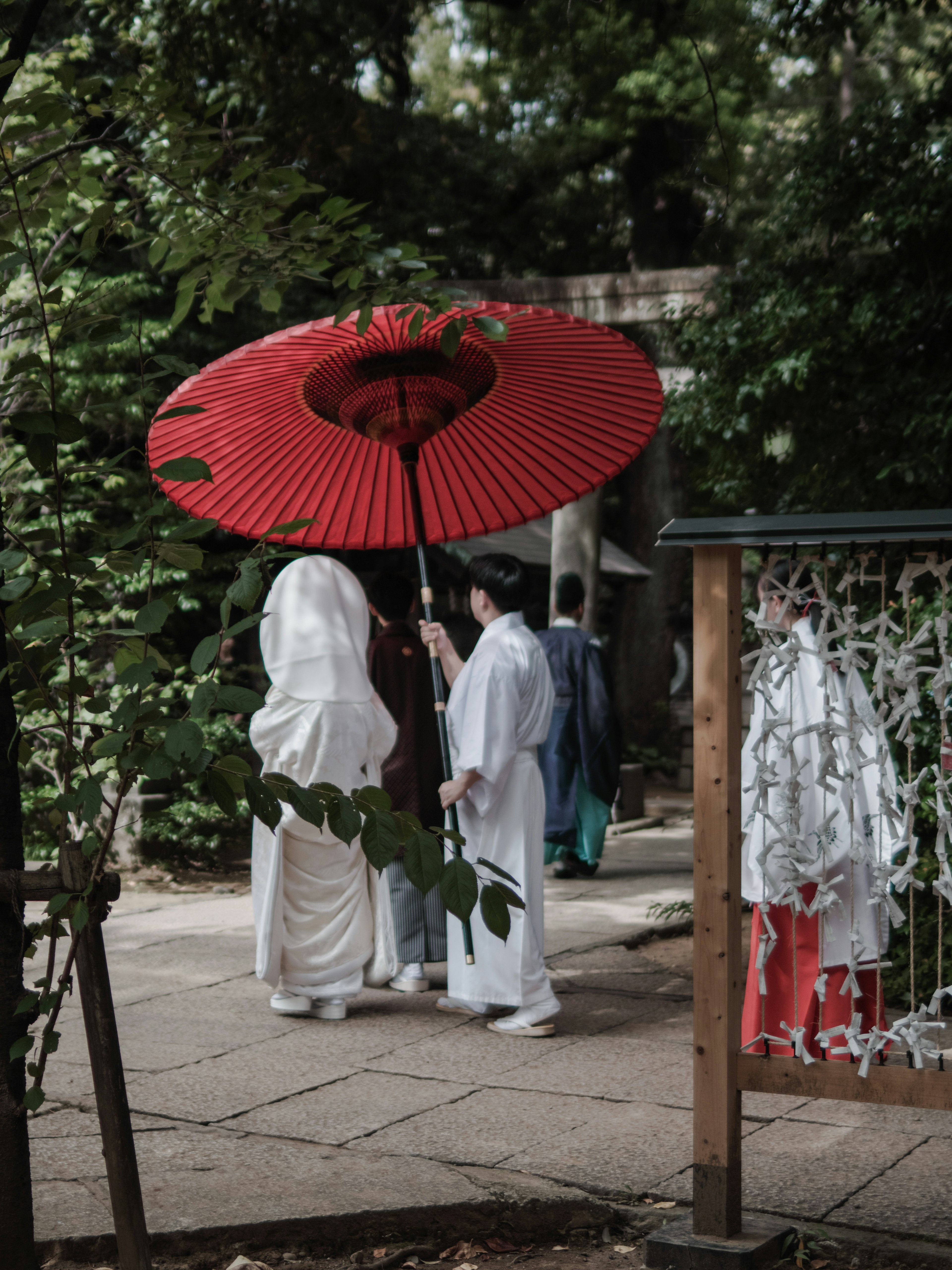 A person in a white kimono holding a red umbrella in a serene outdoor setting