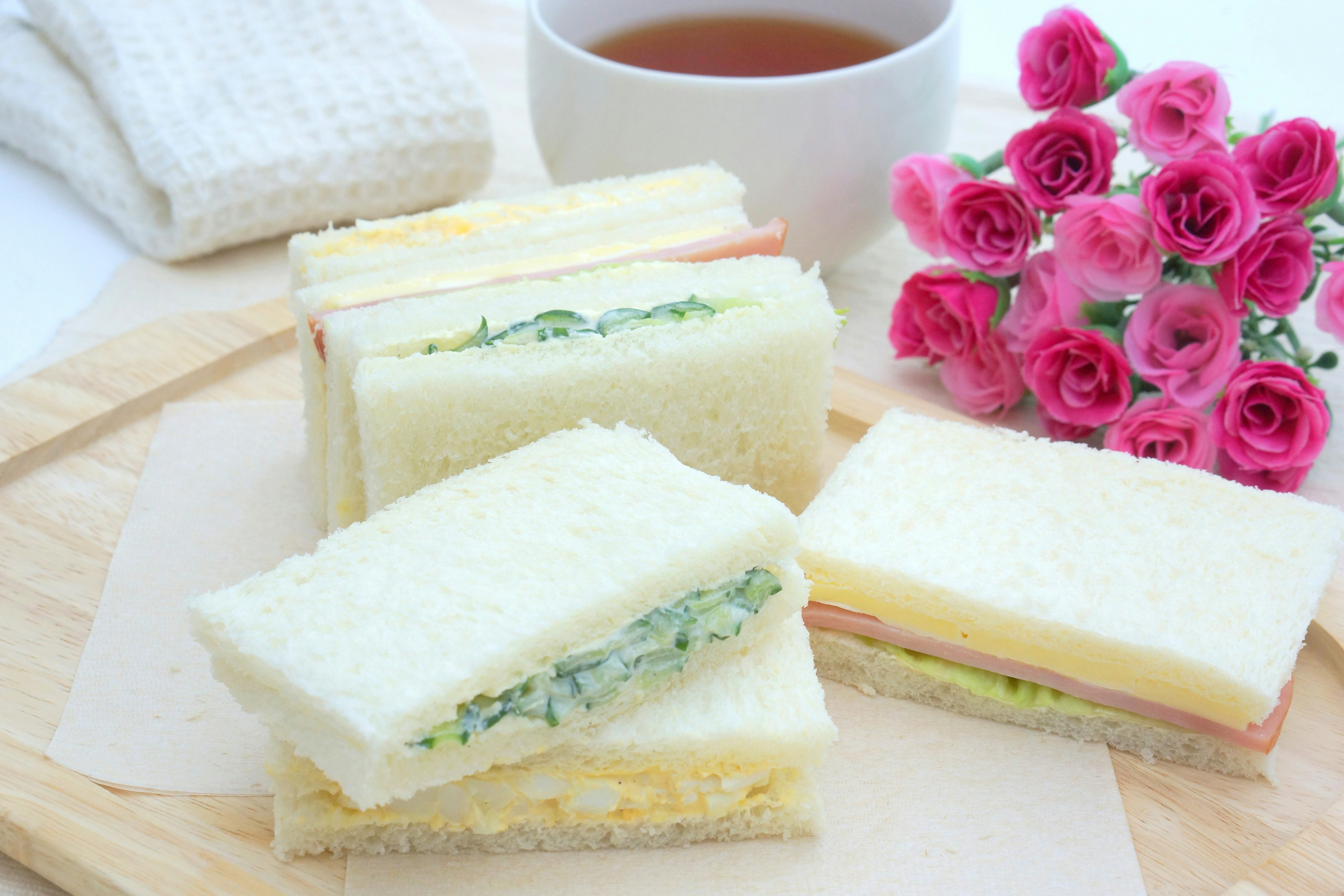 Một đĩa sandwich nhiều lớp với một tách trà và một bó hoa hồng màu hồng