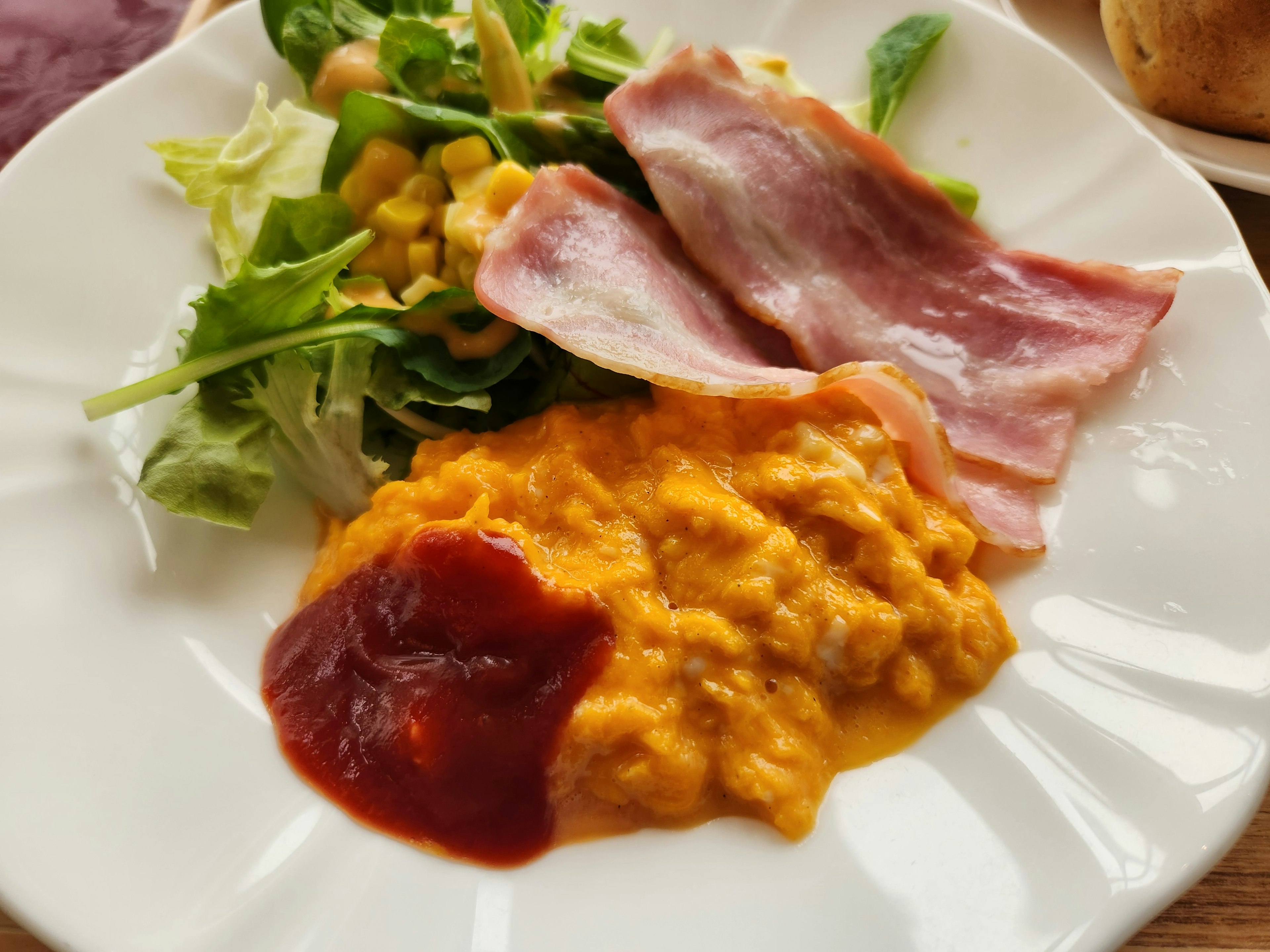 Un plato con ensalada, tocino, huevos revueltos y ketchup