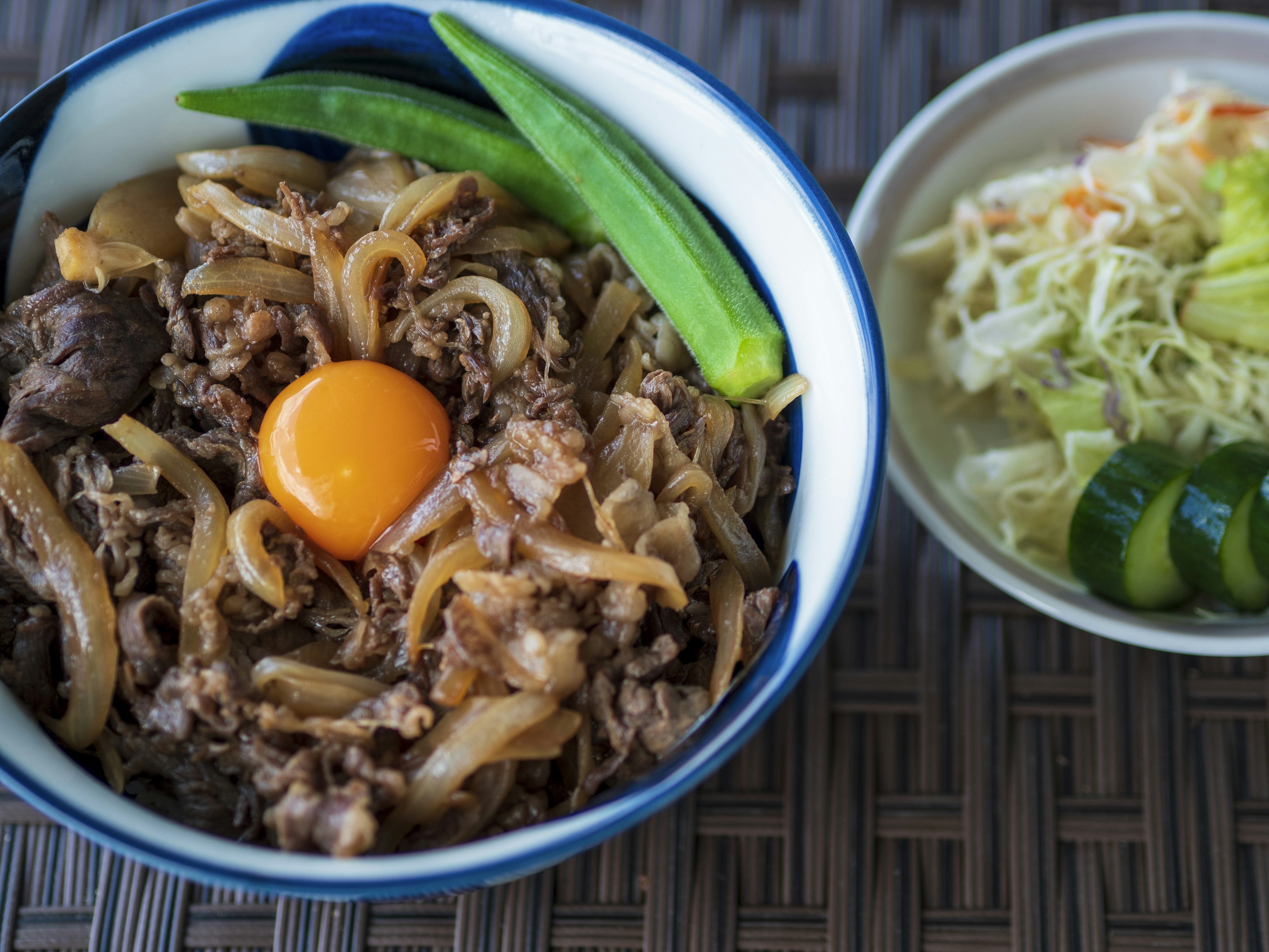 牛肉と玉ねぎの丼に生卵が乗り、横にサラダが添えられた美味しそうな料理