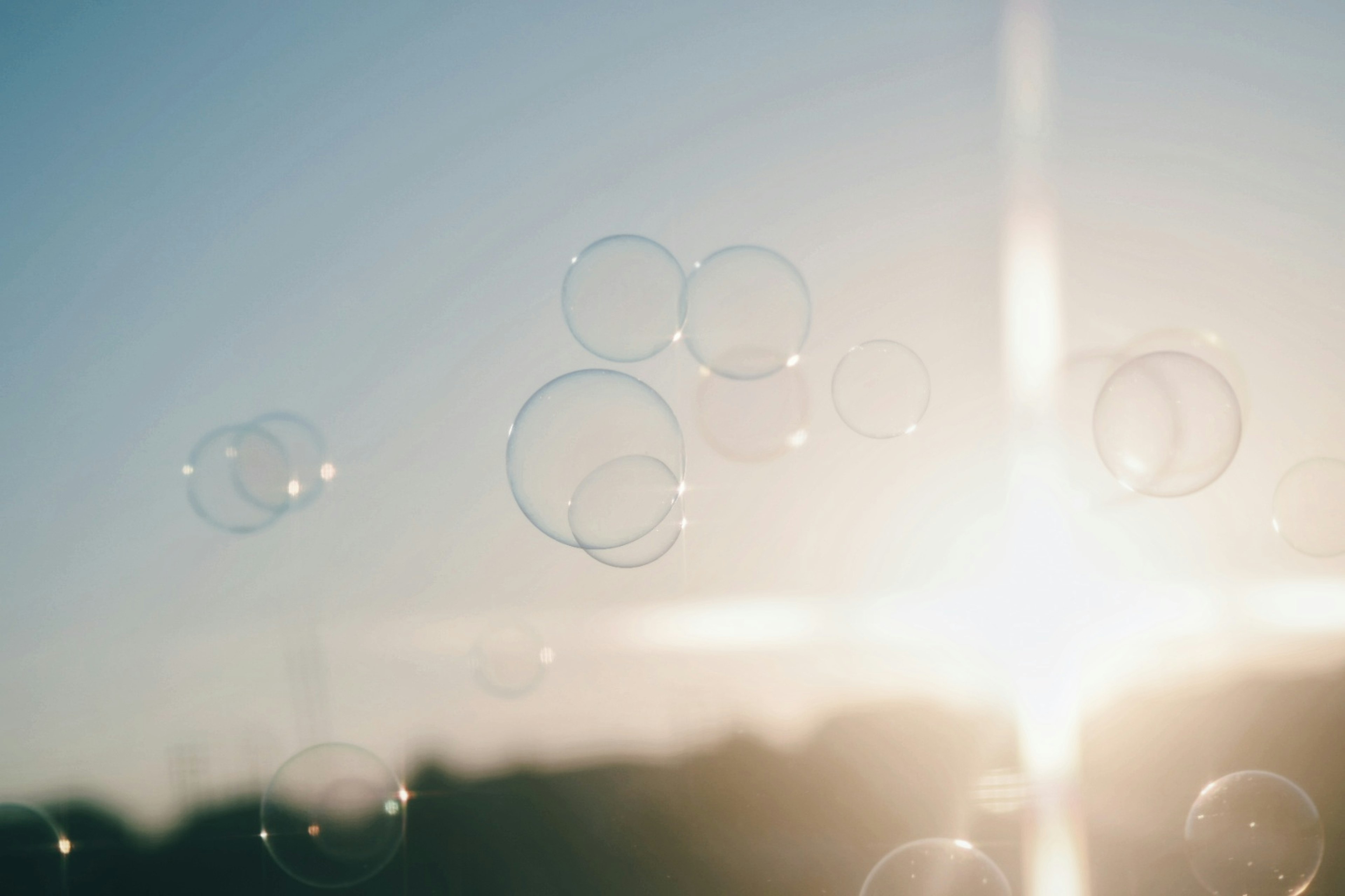 Bubbles floating in the sky with a bright sun in the background