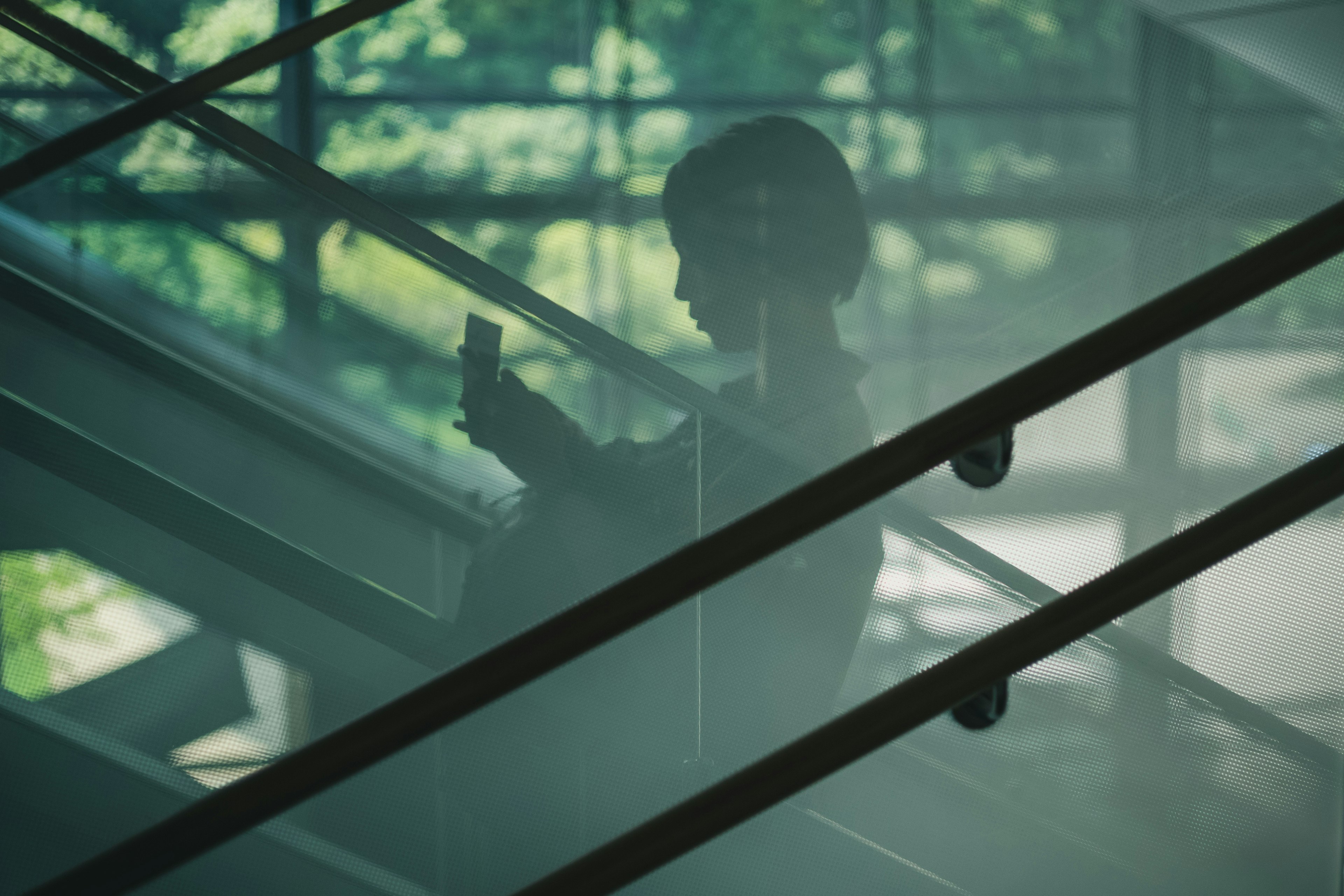 Silhouette d'une femme regardant un smartphone sur un escalier avec des rampes en verre et en métal délicates