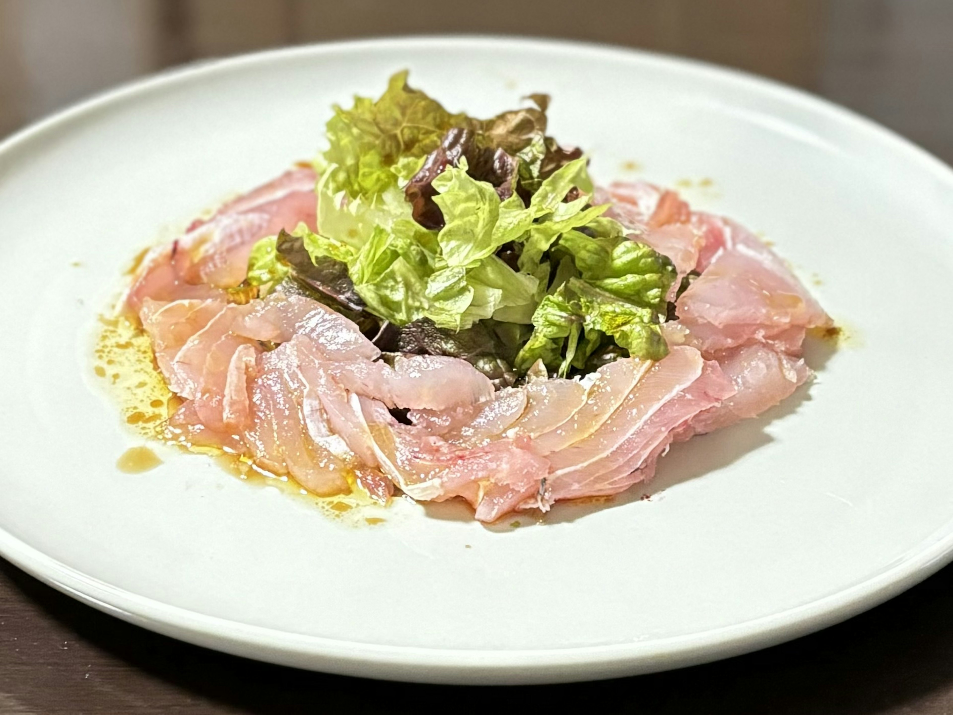 Pescado en rodajas finas con ensalada fresca en un plato blanco