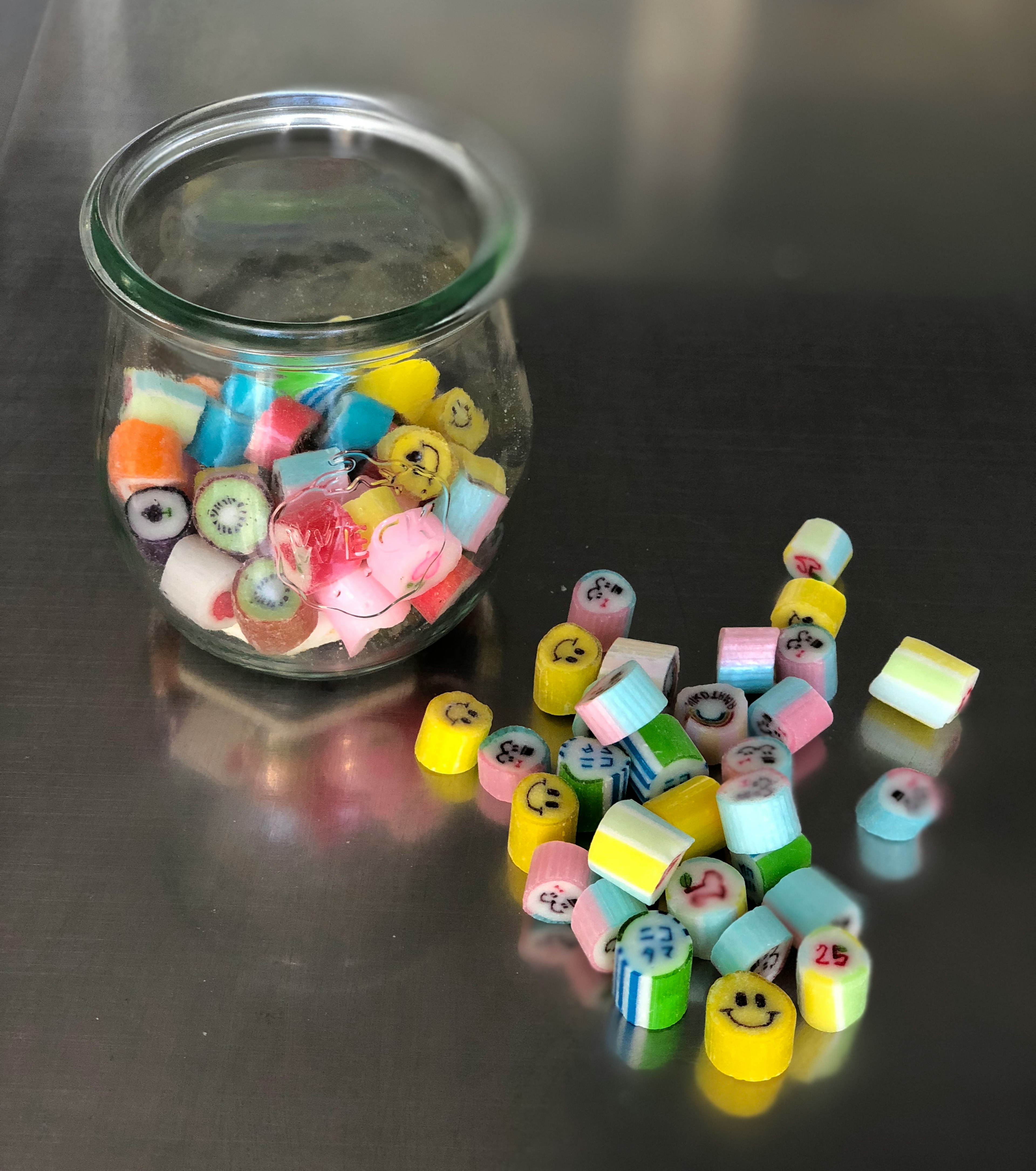 Colorful candies in a glass jar with scattered candies around