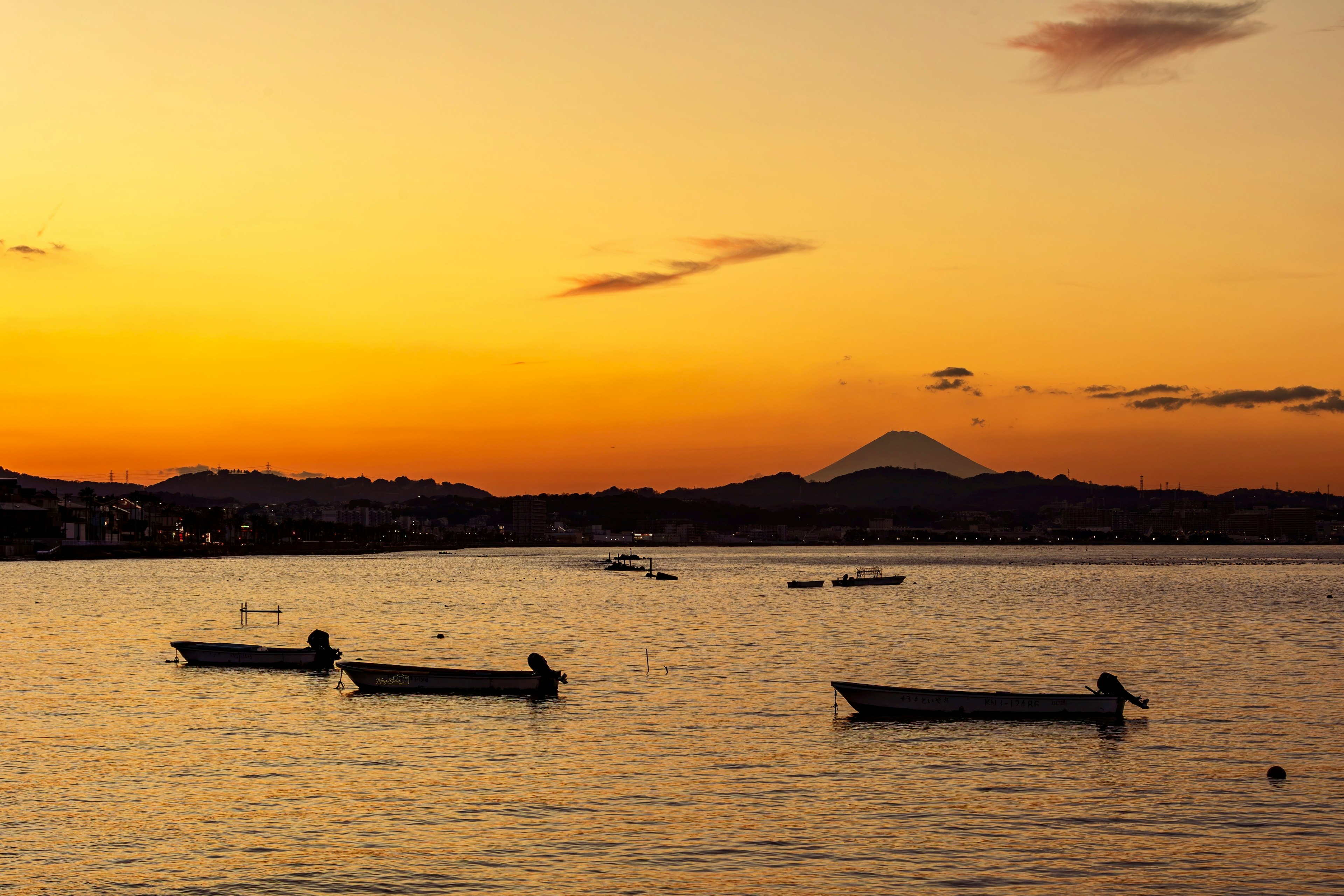 Piccole barche su un mare al tramonto con il monte Fuji sullo sfondo