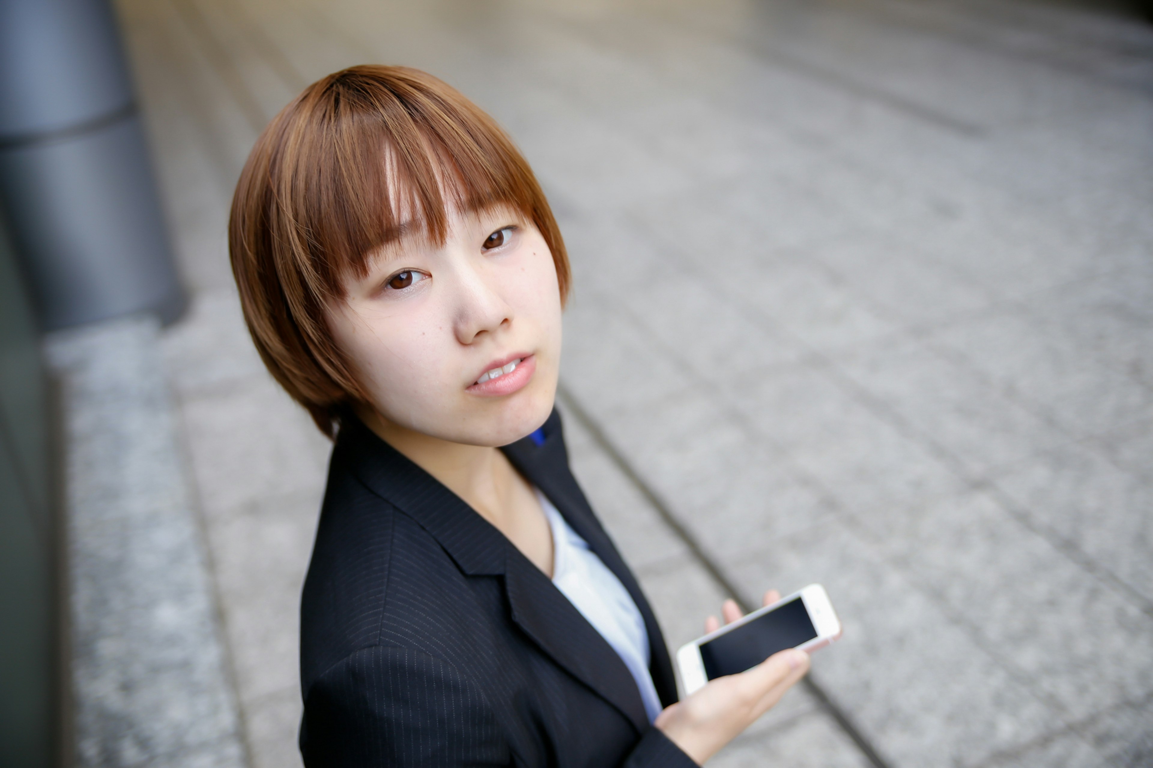 A woman holding a smartphone looking at the camera in an urban setting