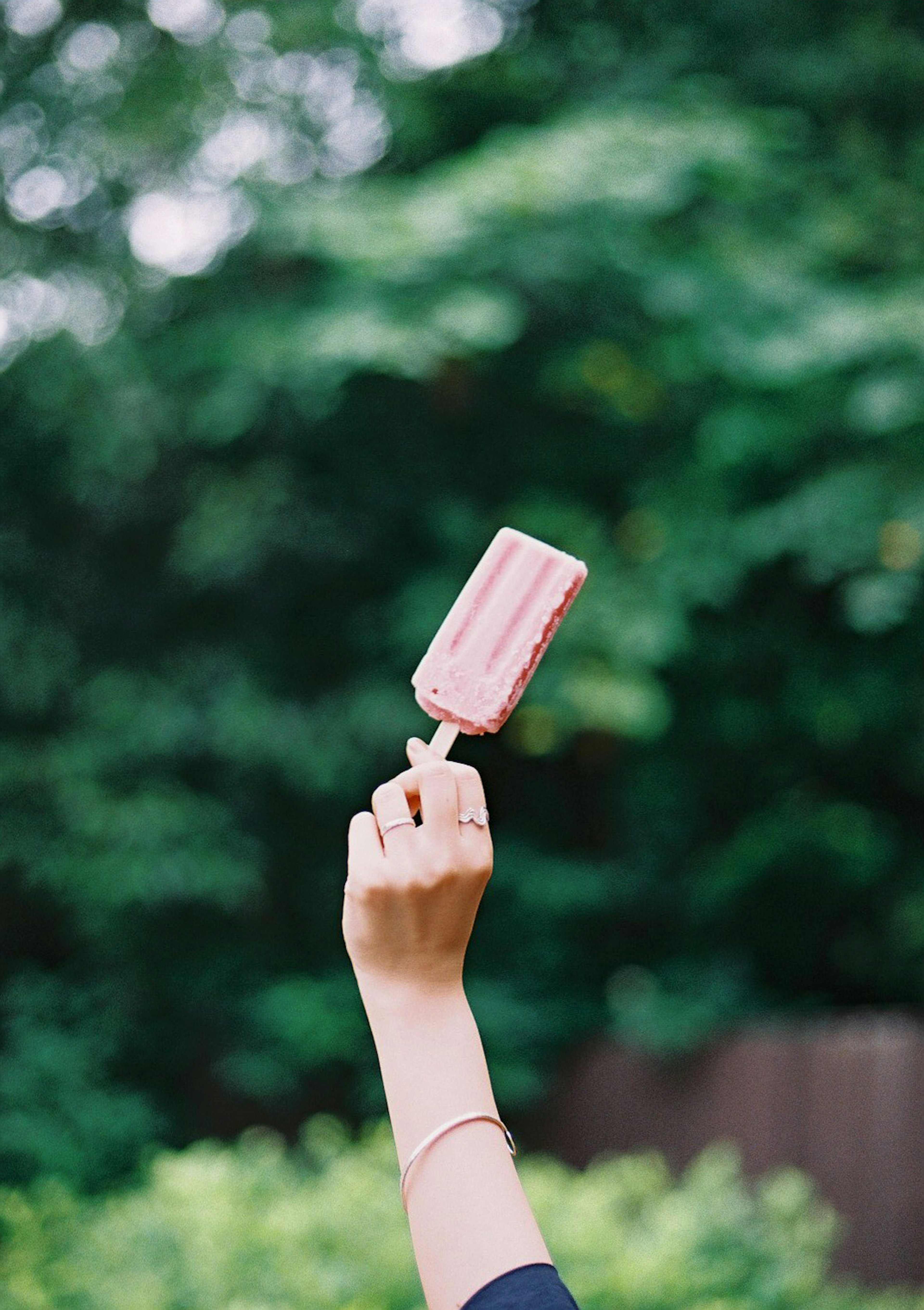 Mano che tiene un gelato rosa contro uno sfondo verde