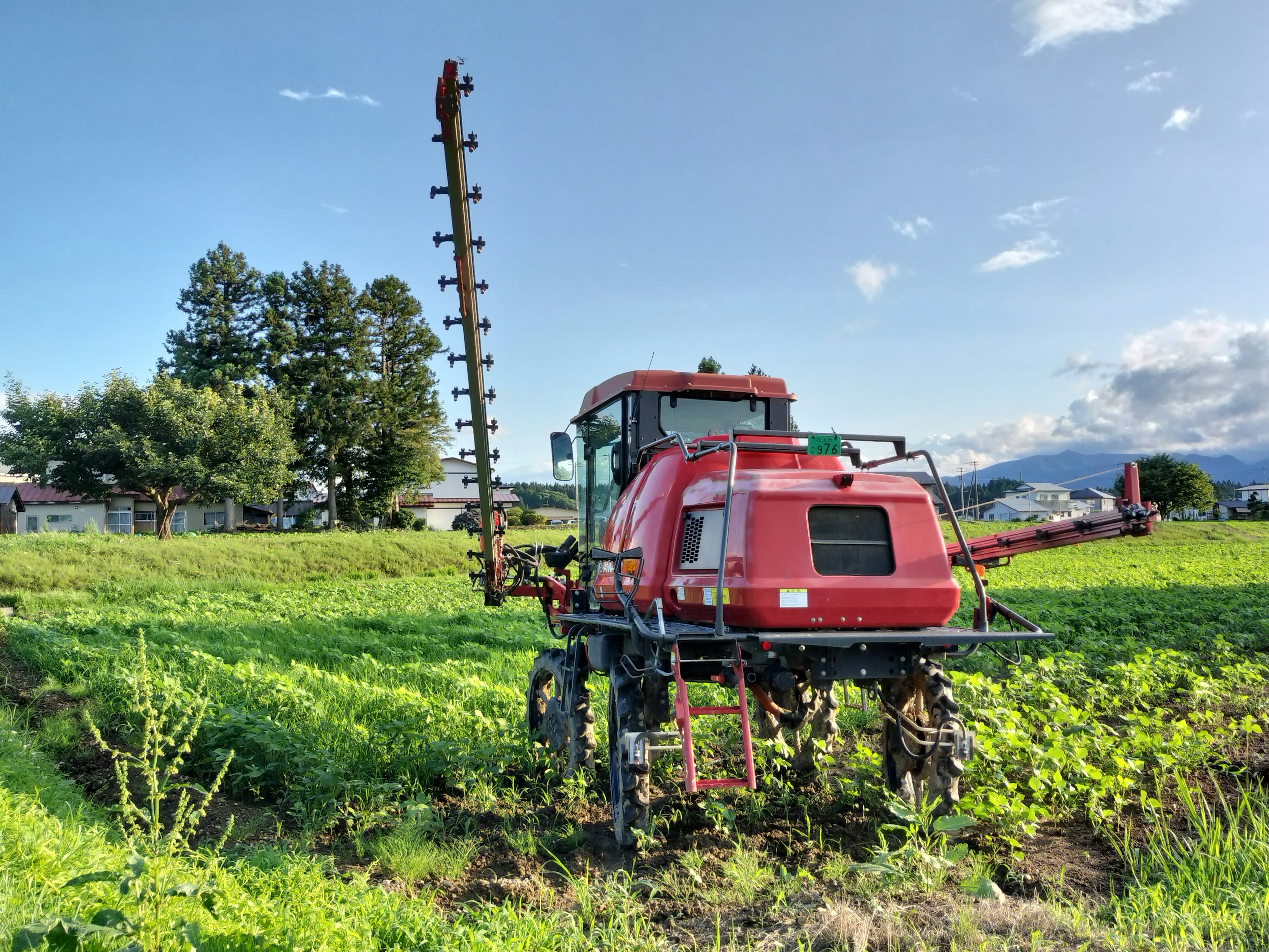 赤い農業機械が緑の畑で作業している風景