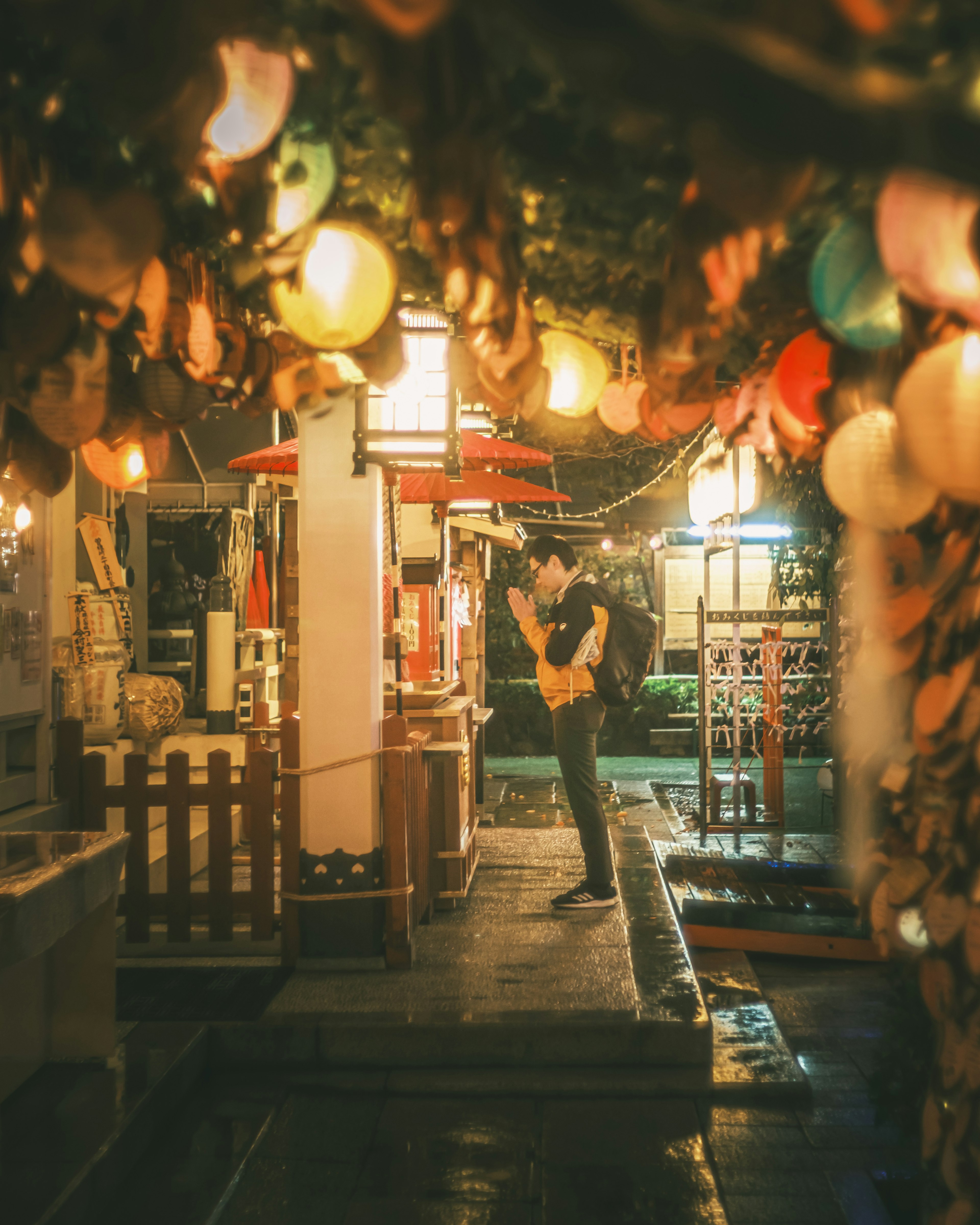 Un homme debout dans un marché nocturne entouré de lanternes colorées et de décorations en coquillage