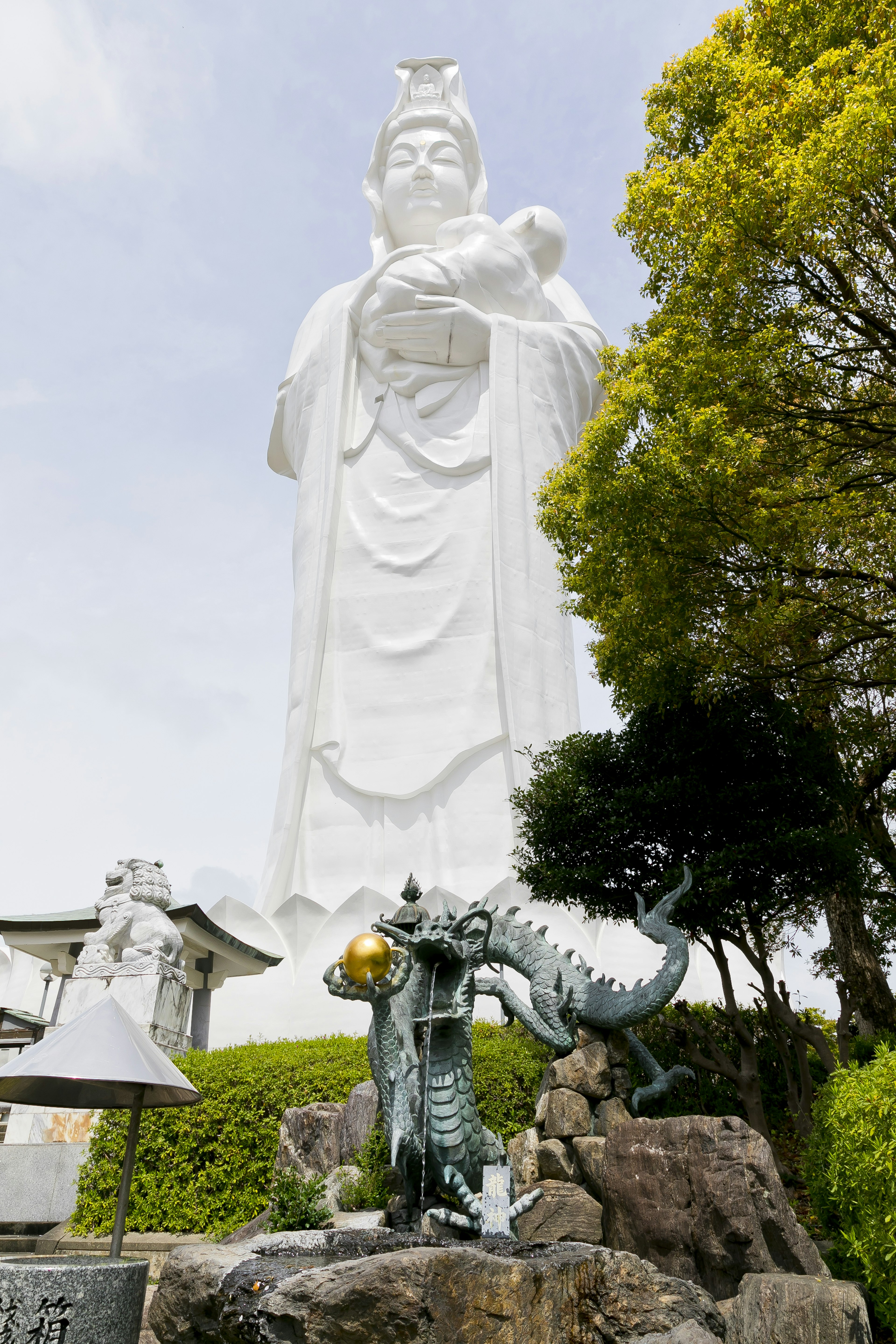 Eine hohe weiße Statue von Kannon mit einer Drachen-Skulptur an der Basis