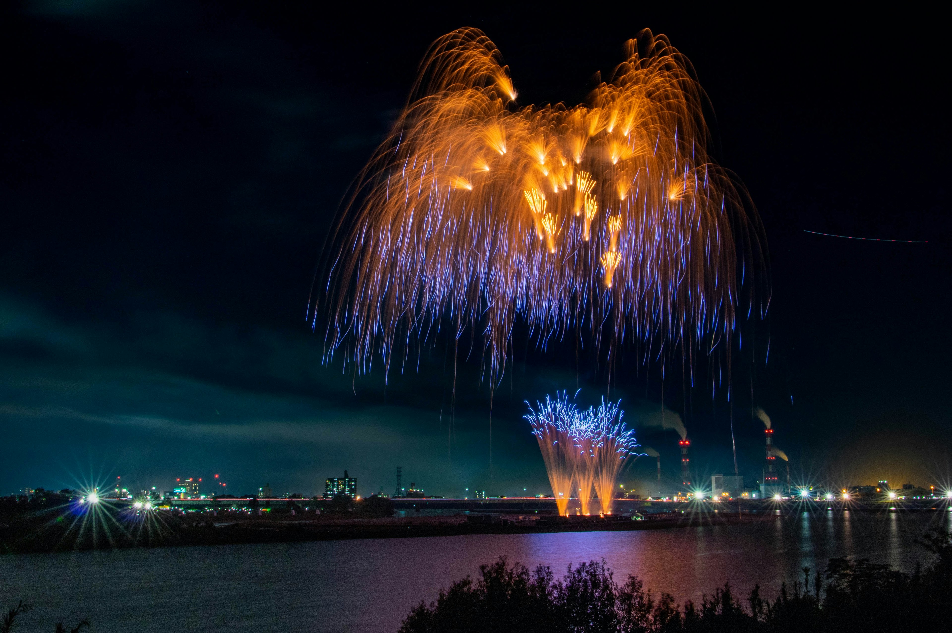 夜空中繽紛的橙色和藍色煙火在河流景觀上空綻放