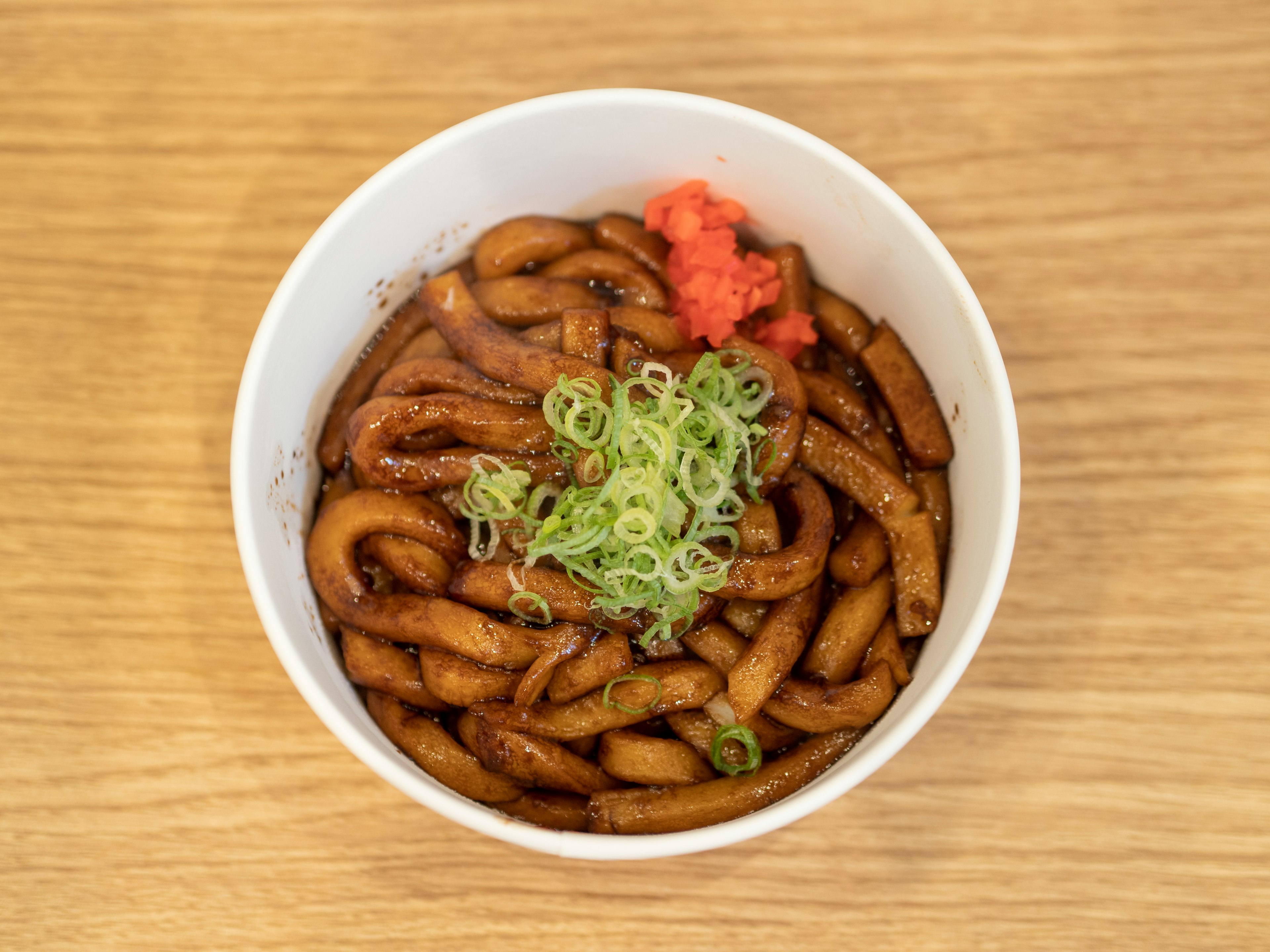 Fideos udon en un tazón blanco cubiertos con cebollines y jengibre encurtido