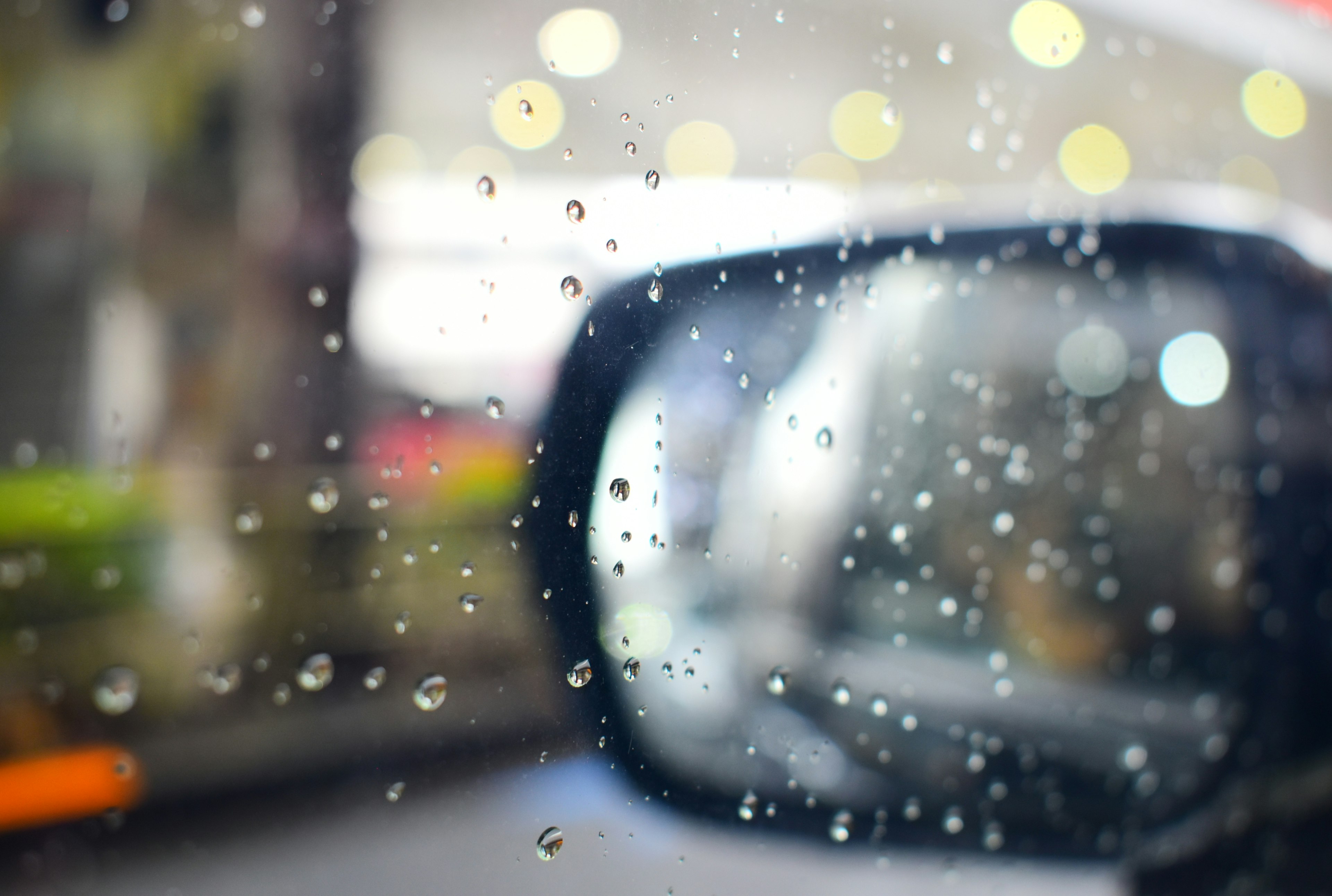 Side mirror of a car with raindrops and a blurred background