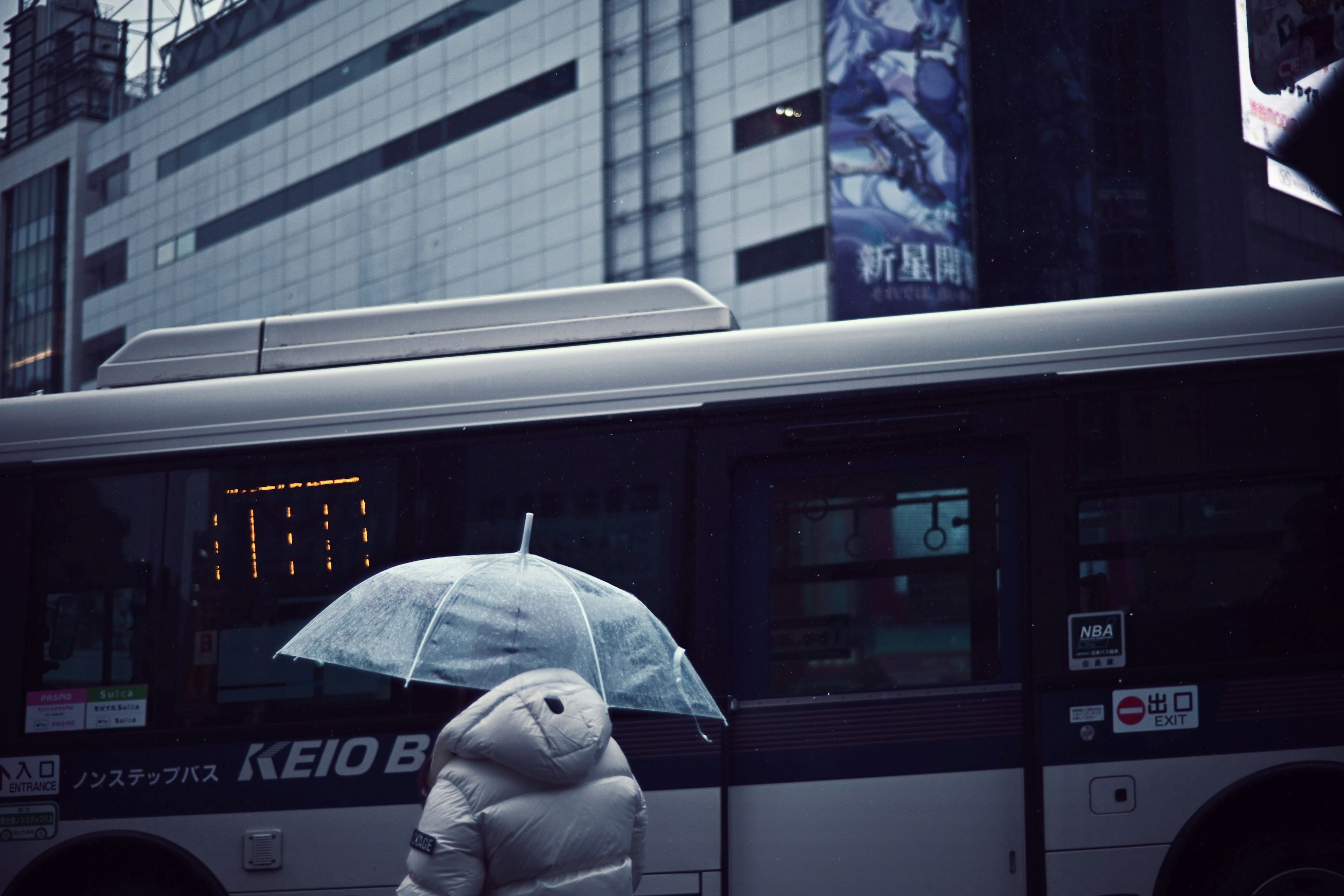 A person with an umbrella walking beside a bus with a building background