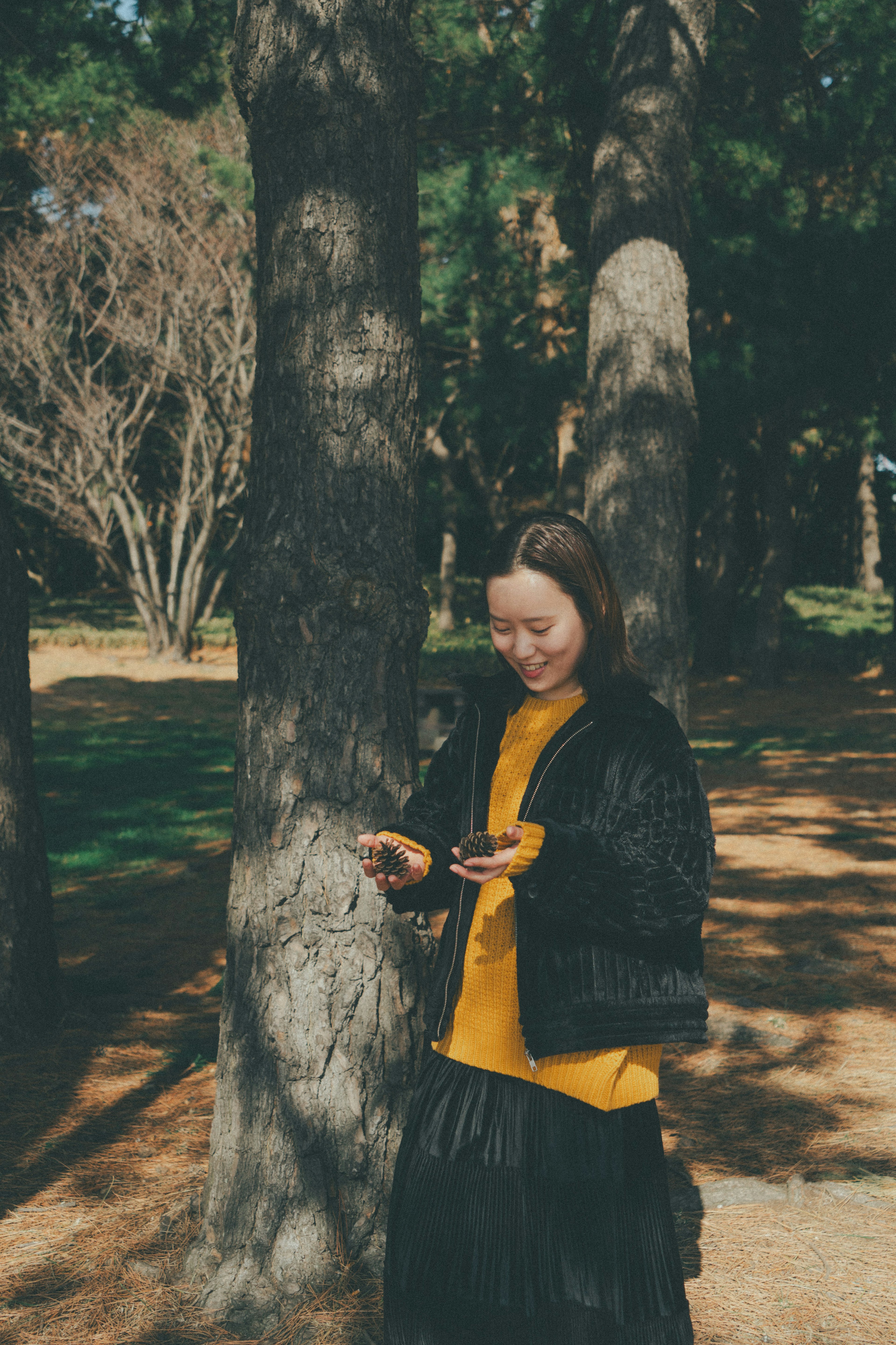 木の近くに立ちスマートフォンを持つ女性の写真