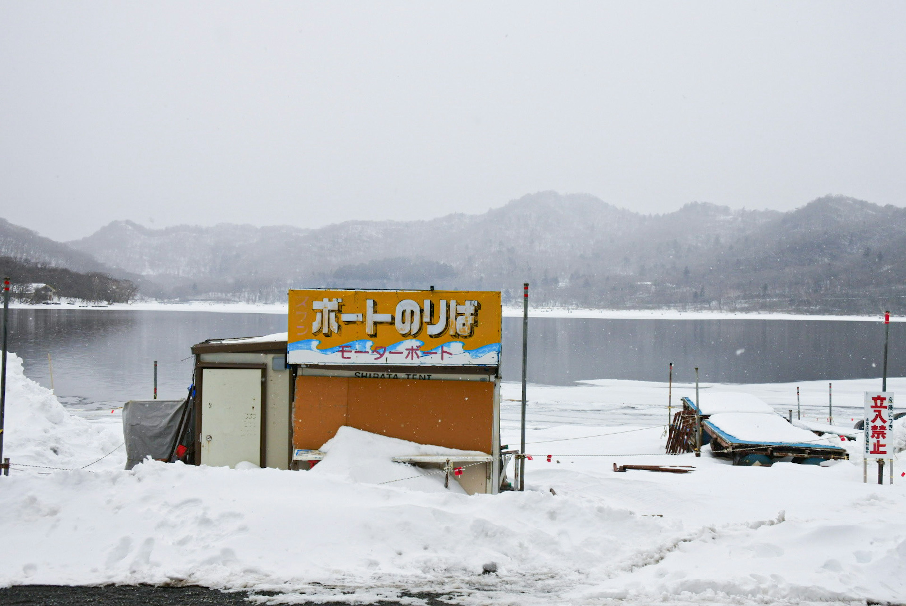 雪に覆われた湖のほとりにある小屋と看板