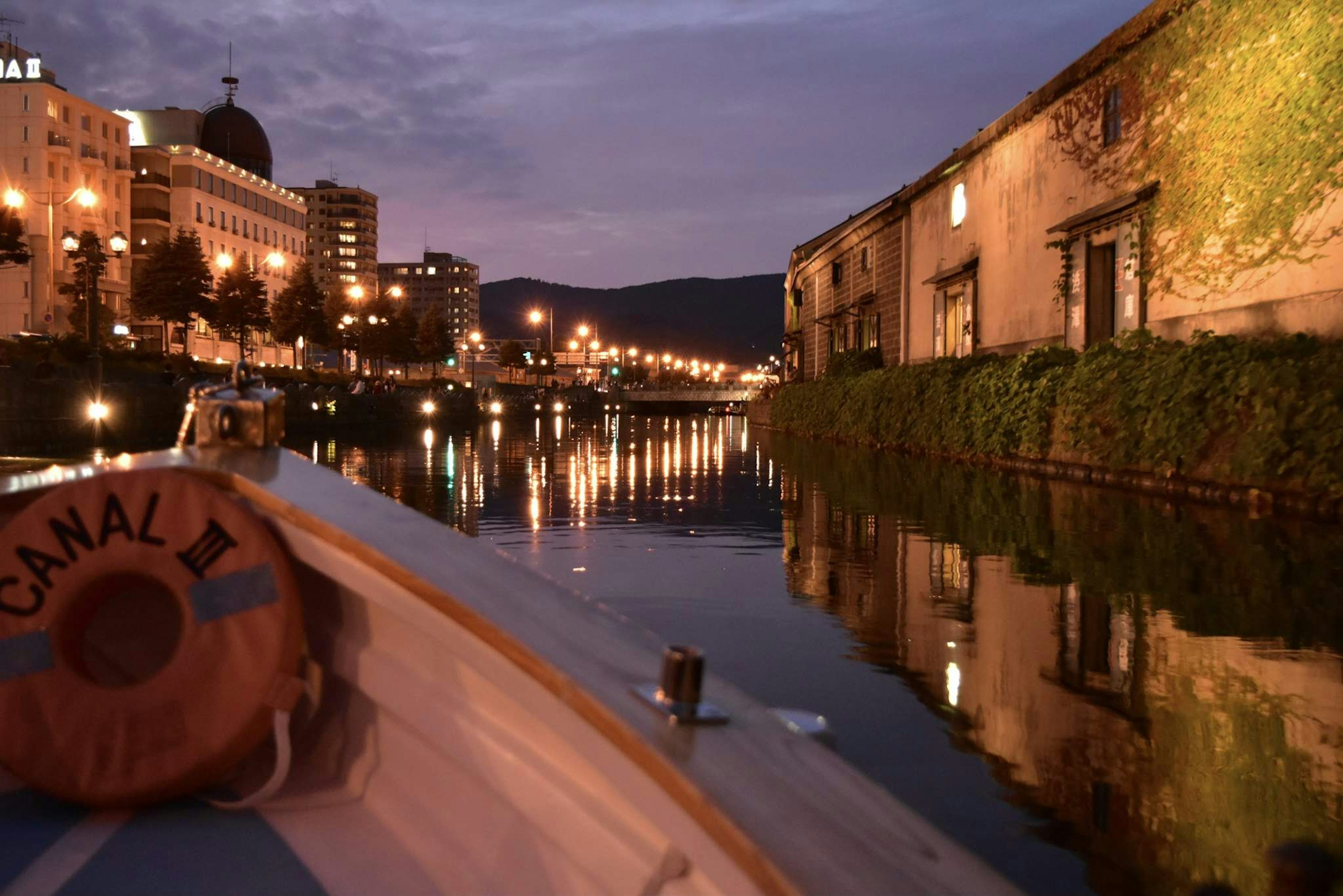 Vista panoramica da una barca su un canale al crepuscolo con riflessi e luci cittadine