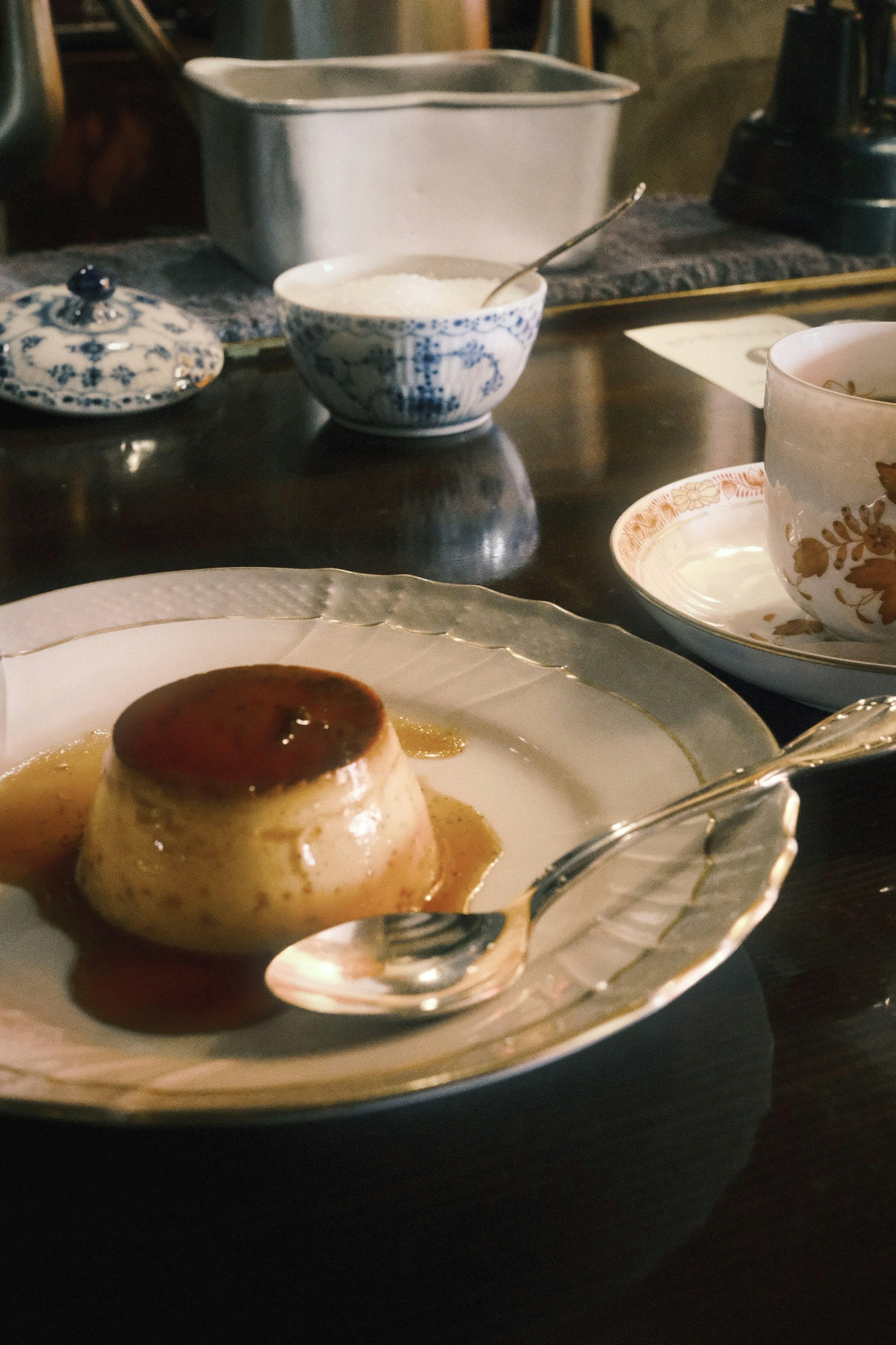 A flan topped with caramel sauce on a decorative plate with a spoon beside it