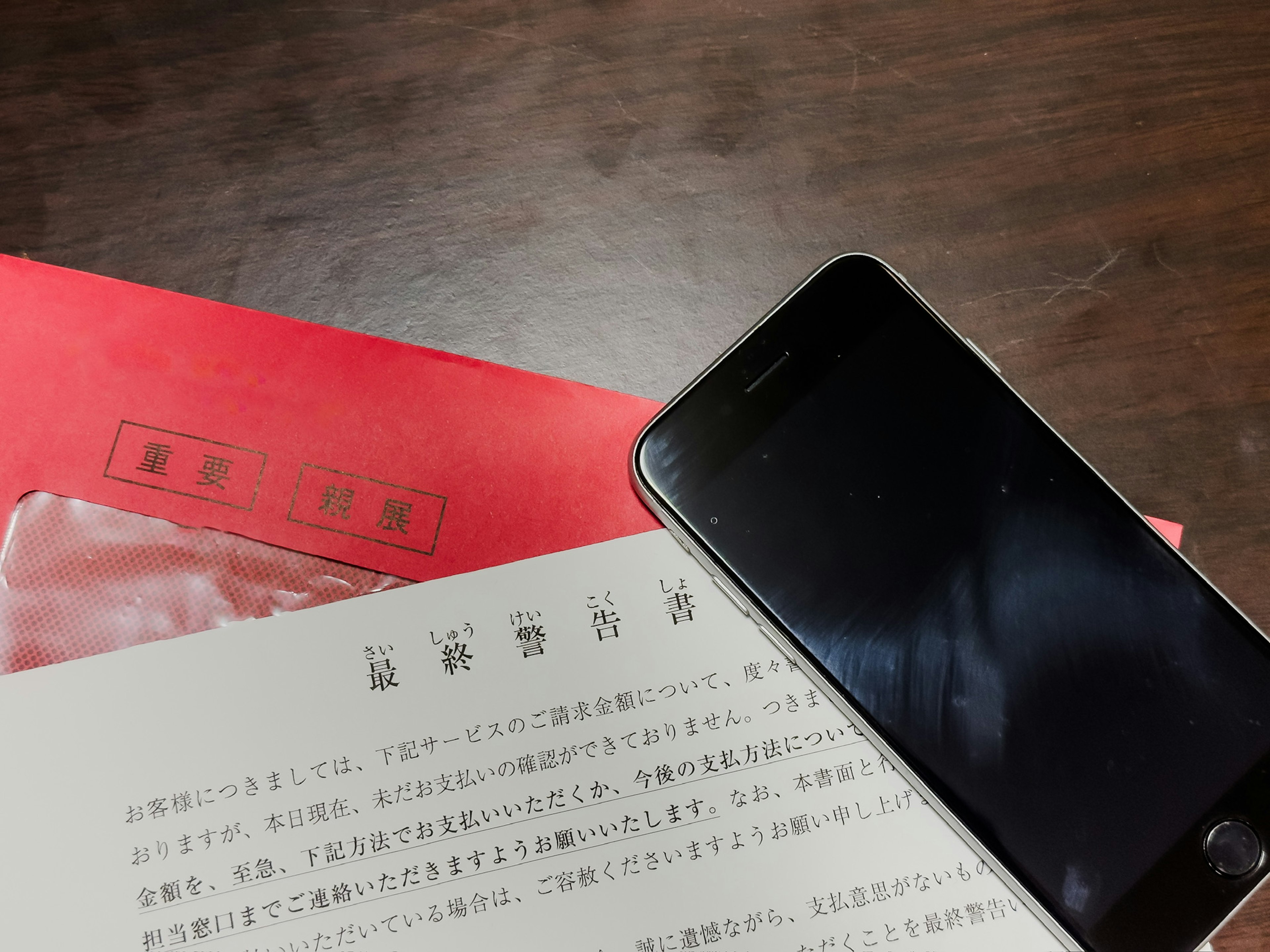 A smartphone rests on a table next to a red envelope and a white document