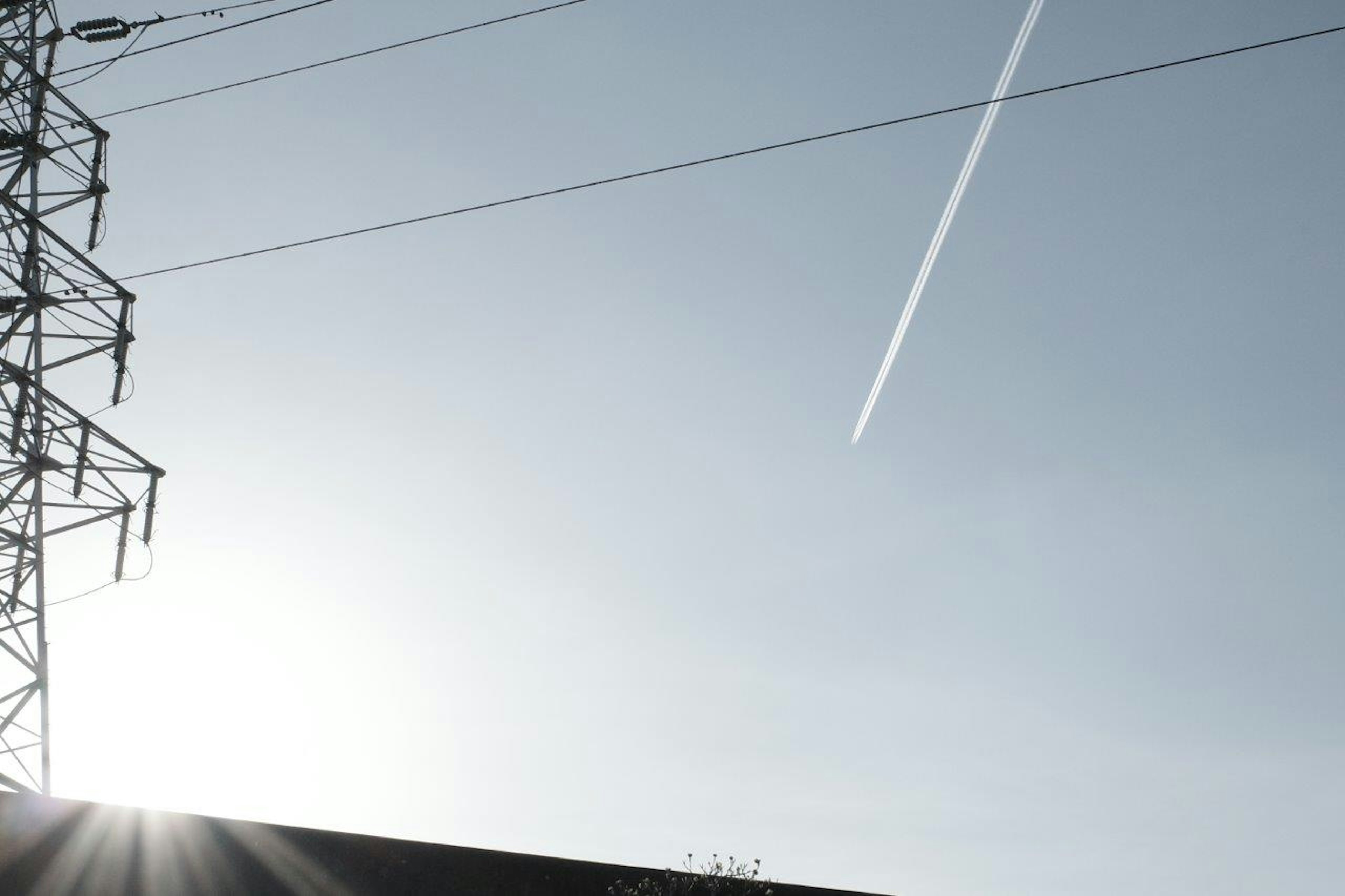 青空に飛行機雲と電柱が見える風景