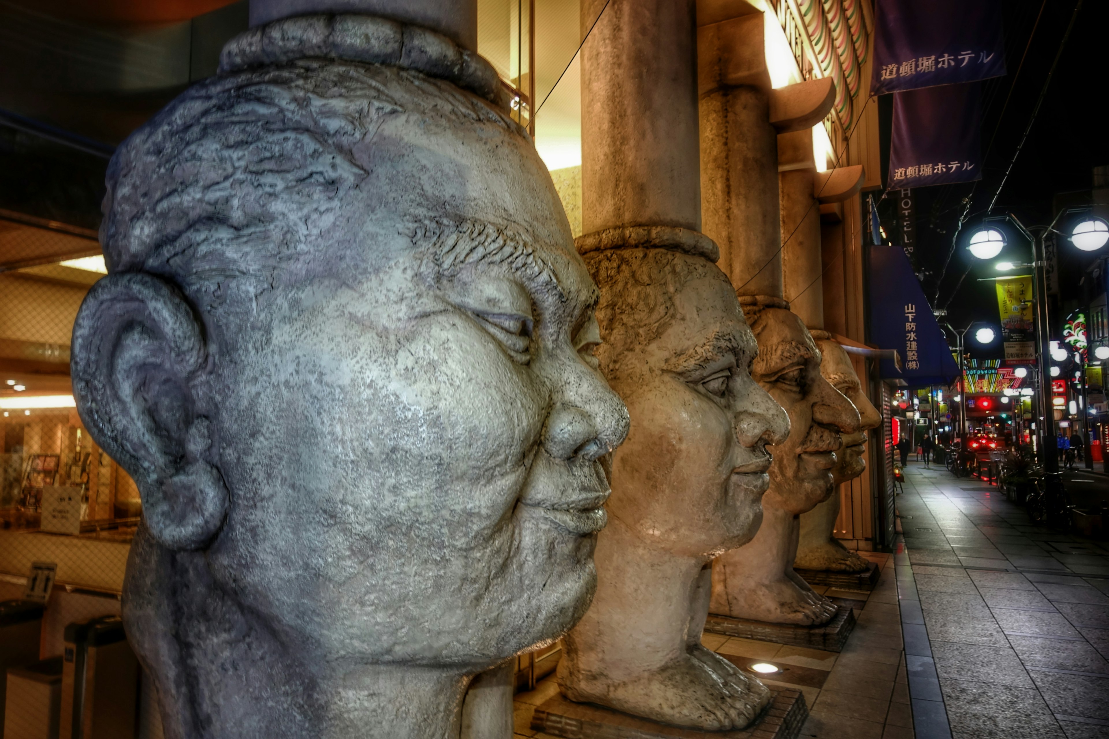 Steinskulpturen von Gesichtern in einer Nachtstraße aufgereiht