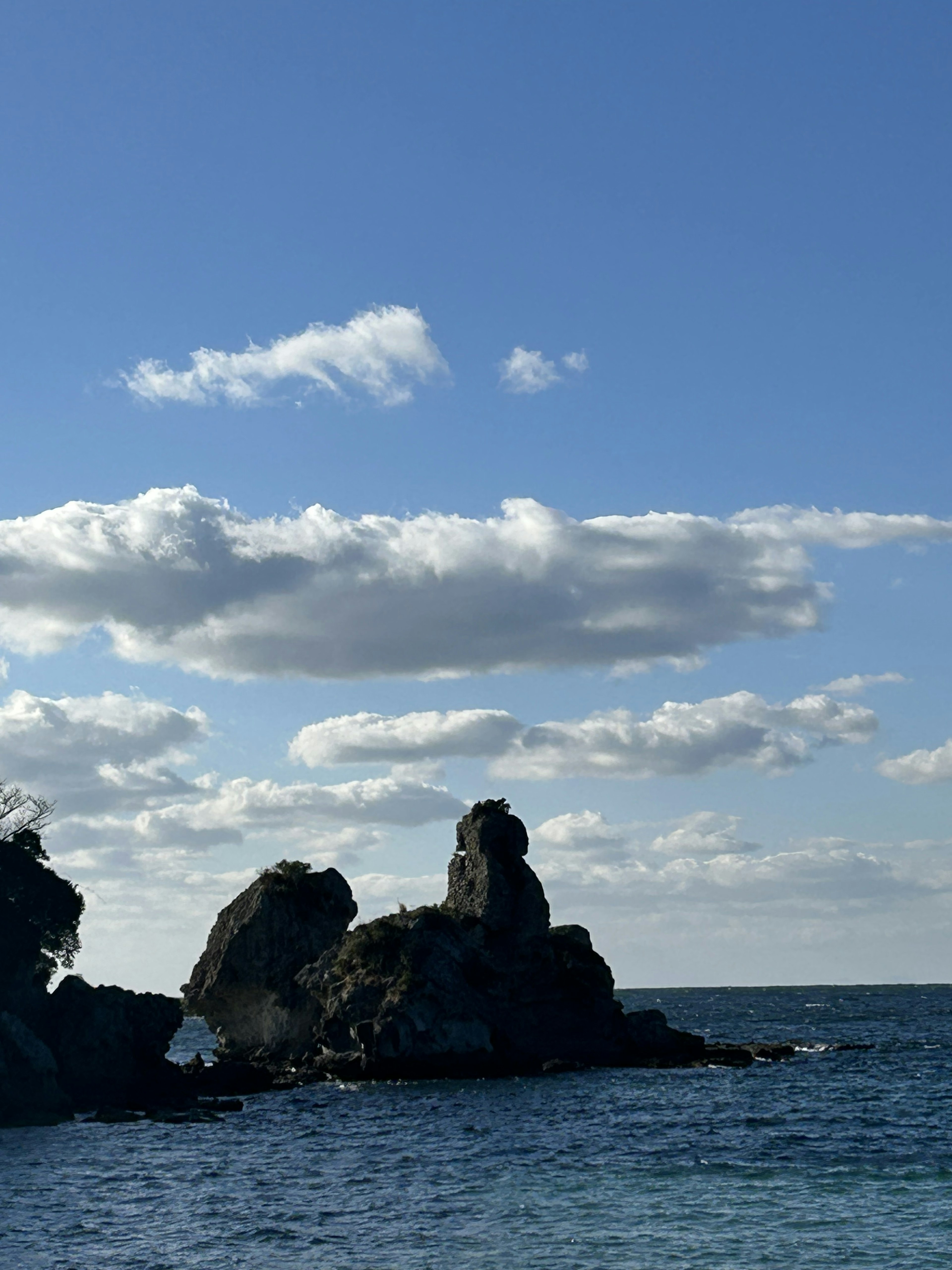 Rock formations in the ocean under a blue sky with clouds