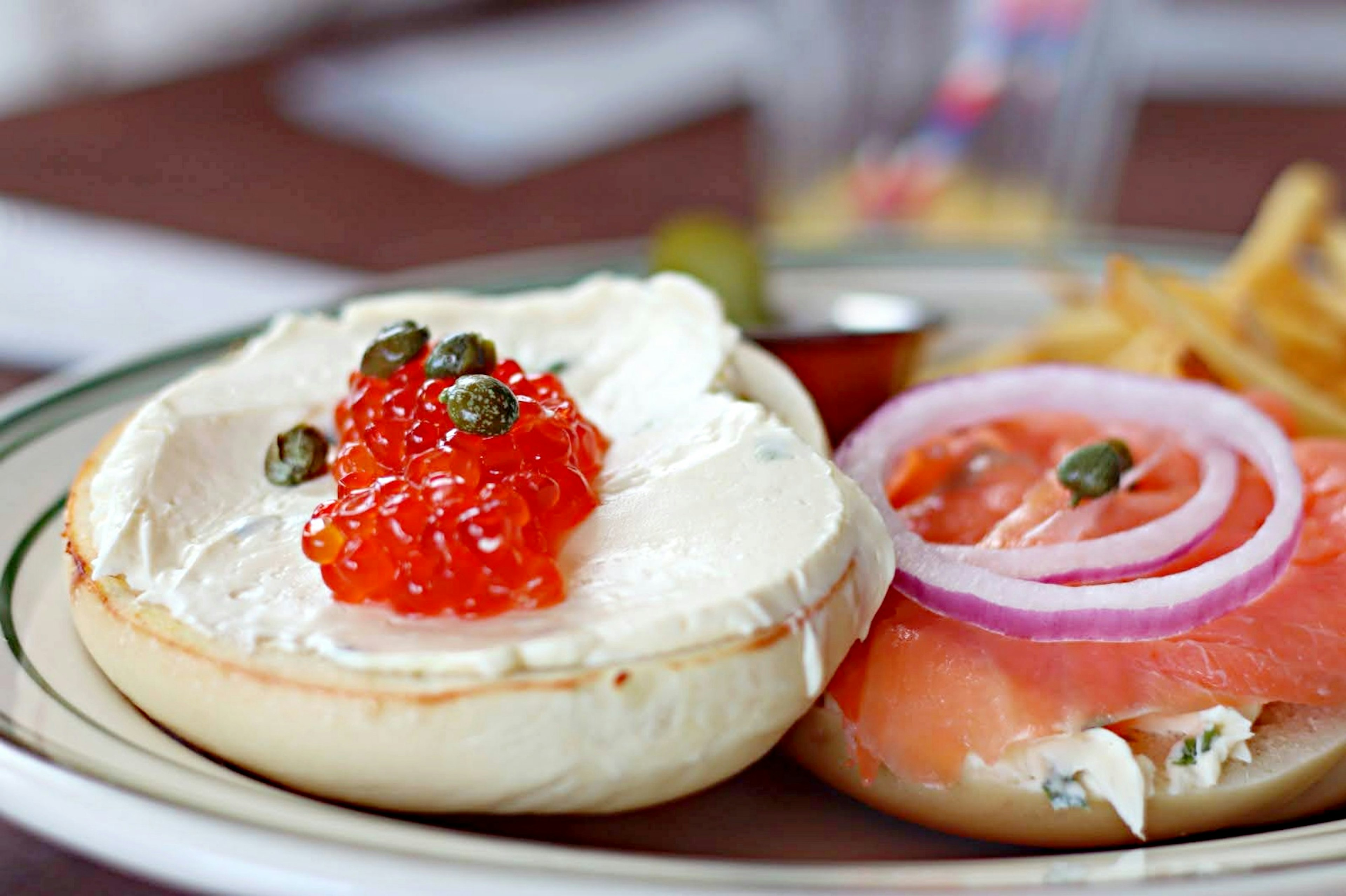 Bagel con crema di formaggio guarnito con caviale rosso e fette di cipolla rossa accanto a salmone affumicato