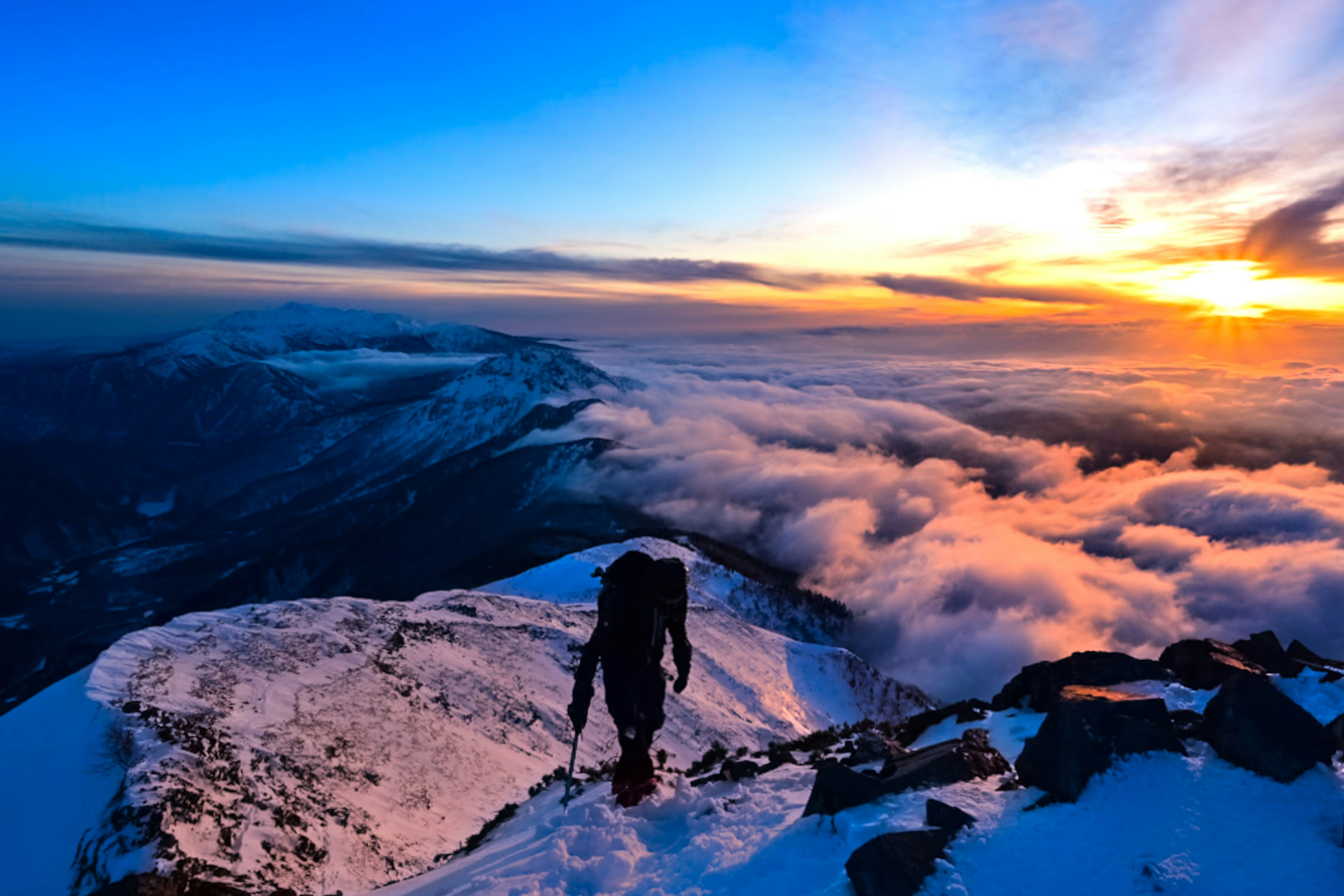 Ein Bergsteiger, der den Sonnenuntergang vom verschneiten Gipfel des Berges betrachtet