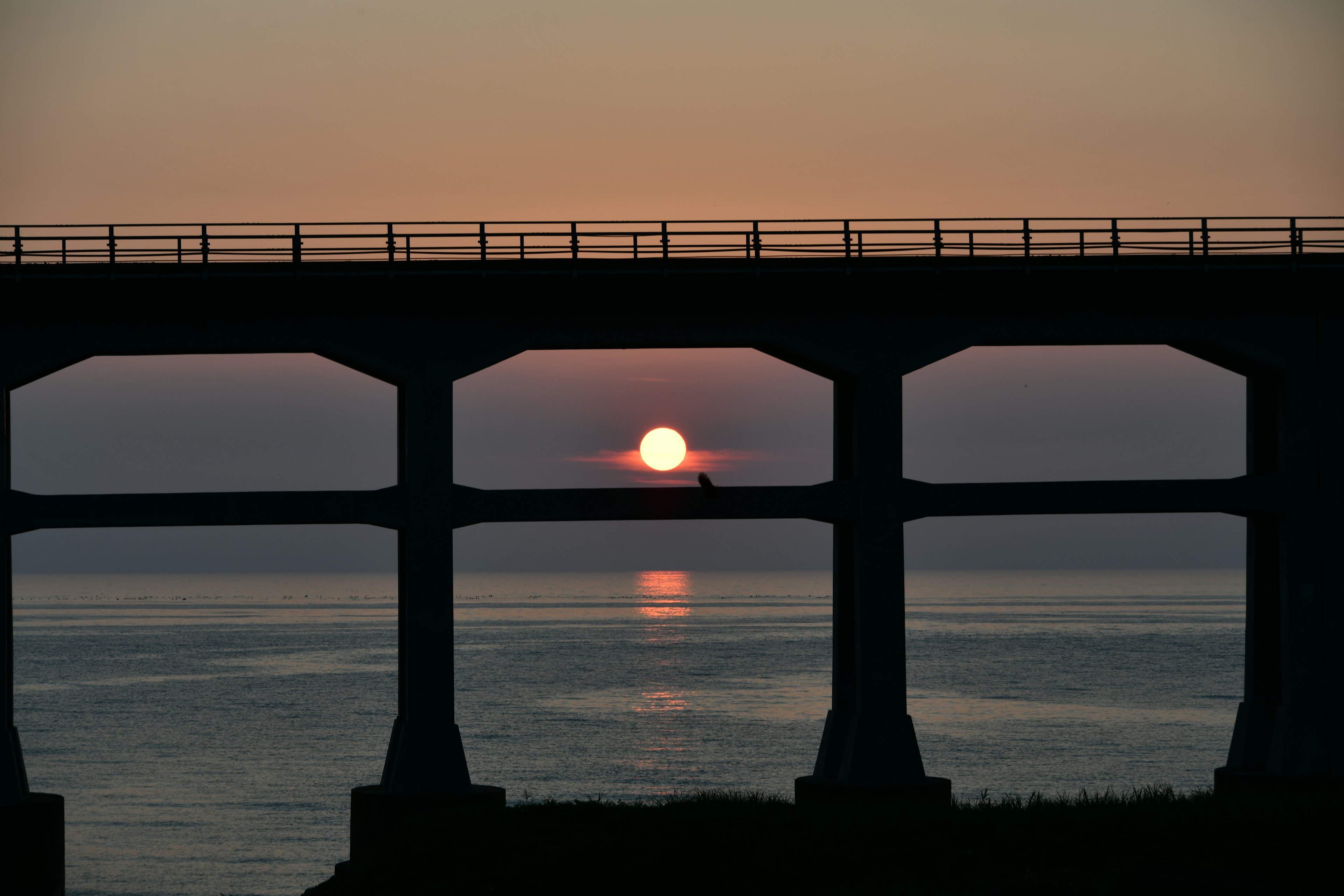 Sunset over the ocean framed by a bridge