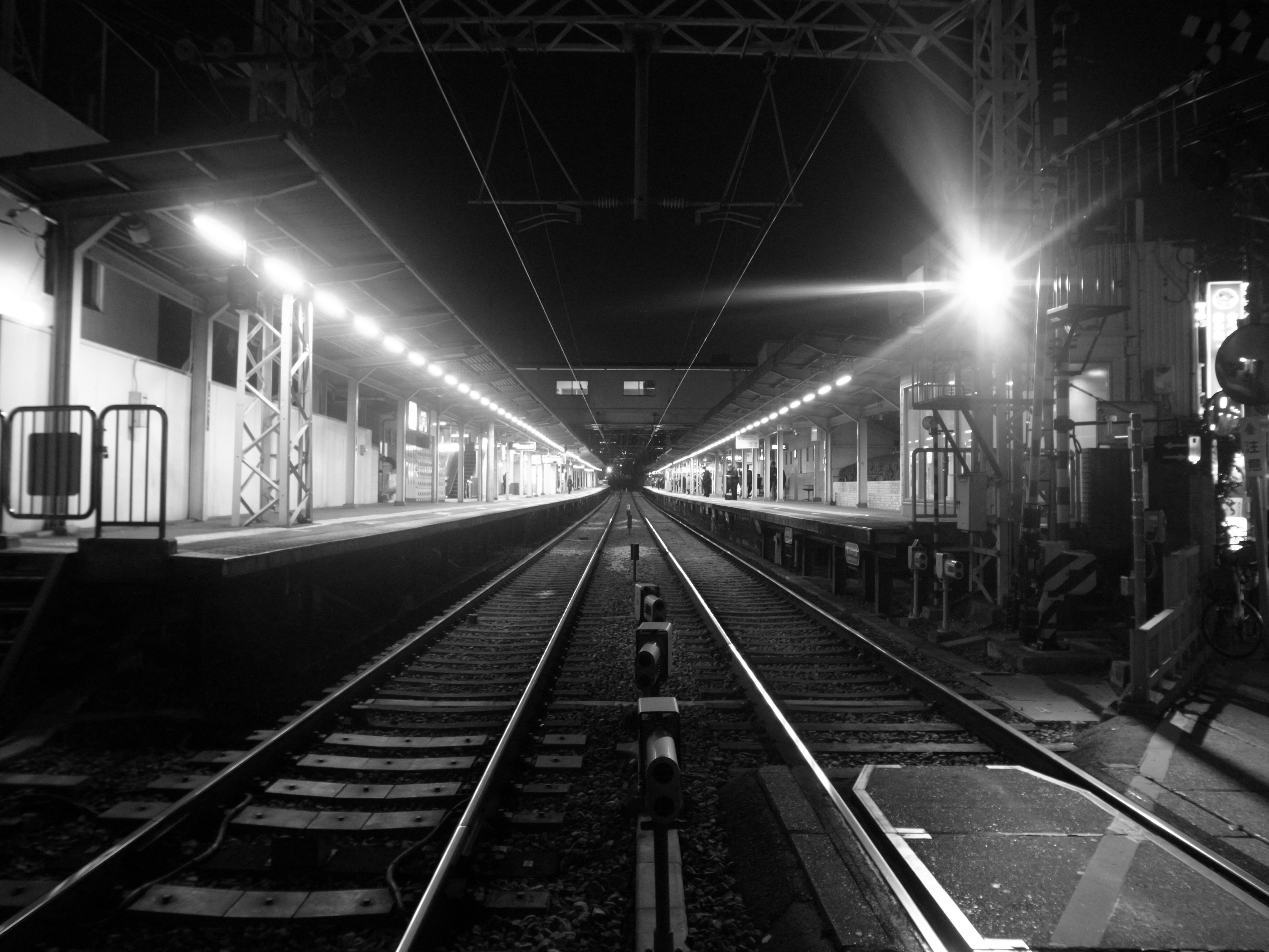 Foto hitam putih rel kereta dan platform di malam hari